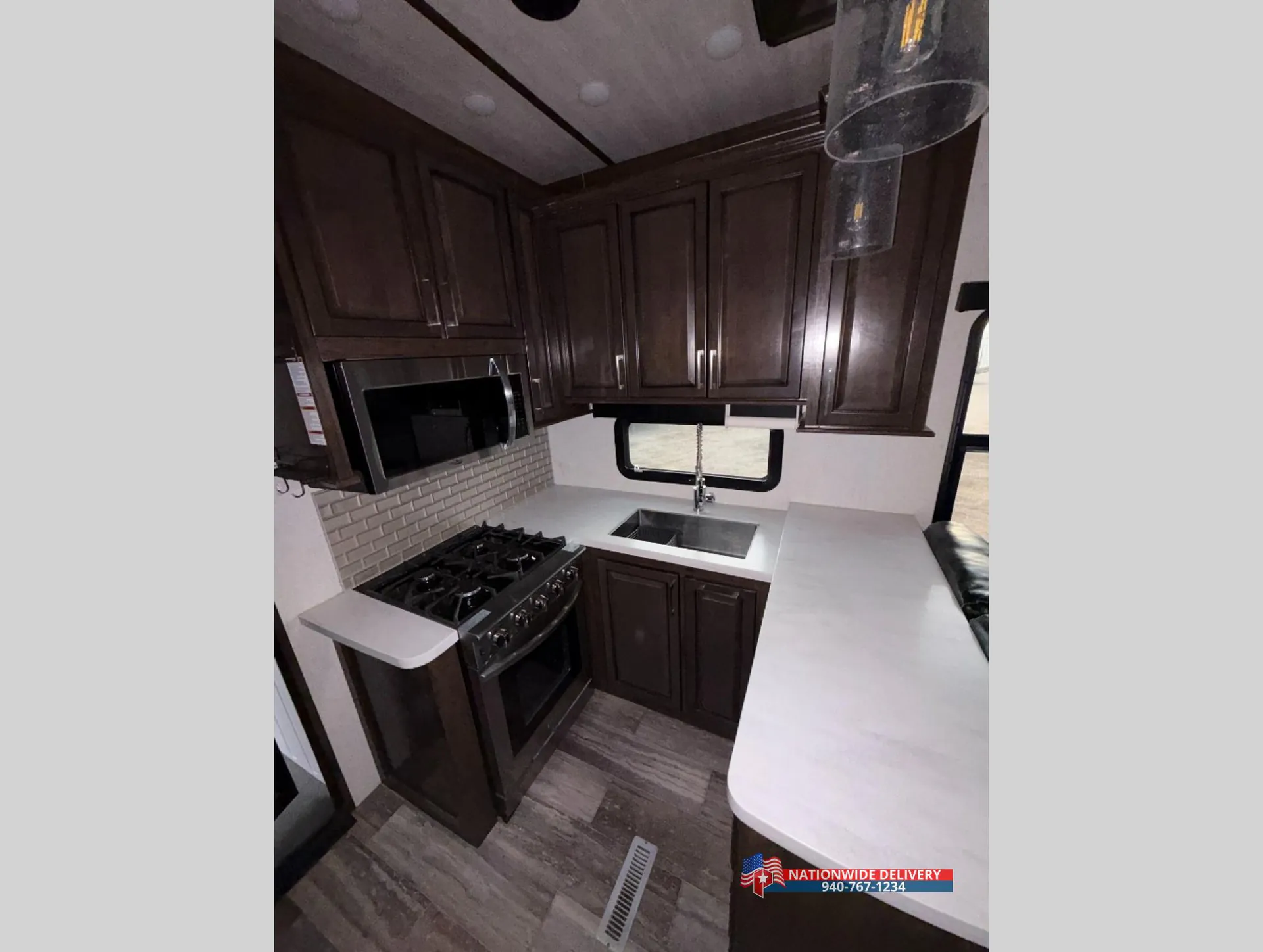 2022 Dutchmen Voltage 4225 — Fifth wheel kitchen with gas range, microwave, sink, countertop, backsplash, and dark overhead cabinetry