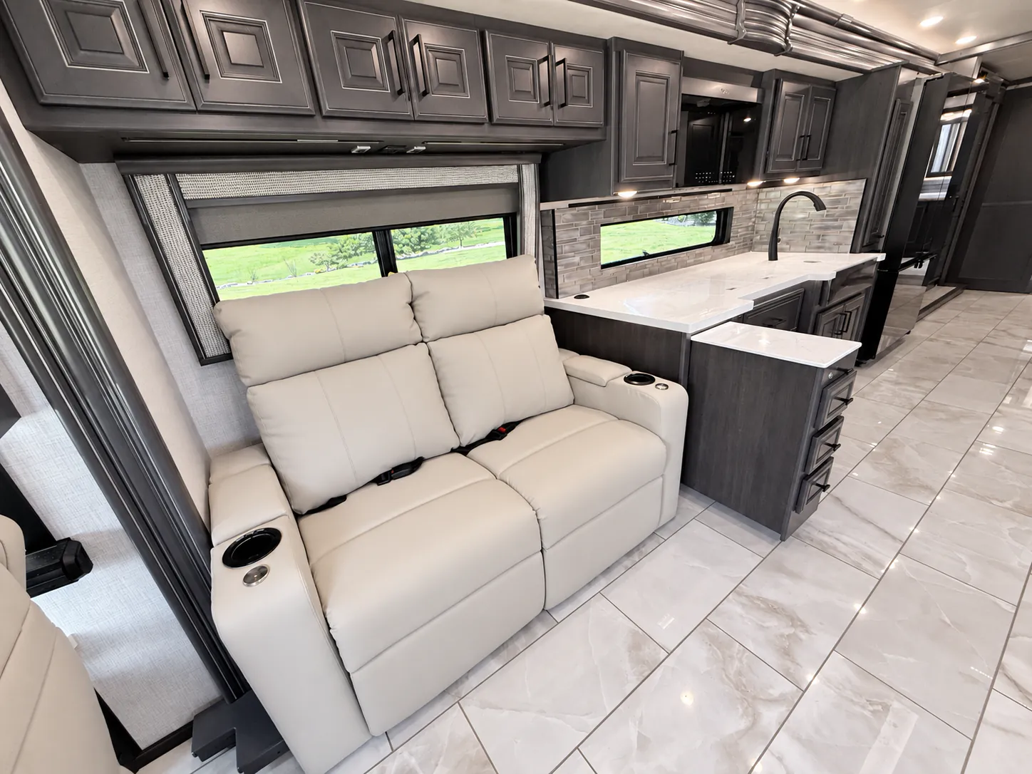2027 Fleetwood Discovery LXE 40M — Kitchen counter with sink, backsplash, drawers, and overhead cabinets beside a powered recliner