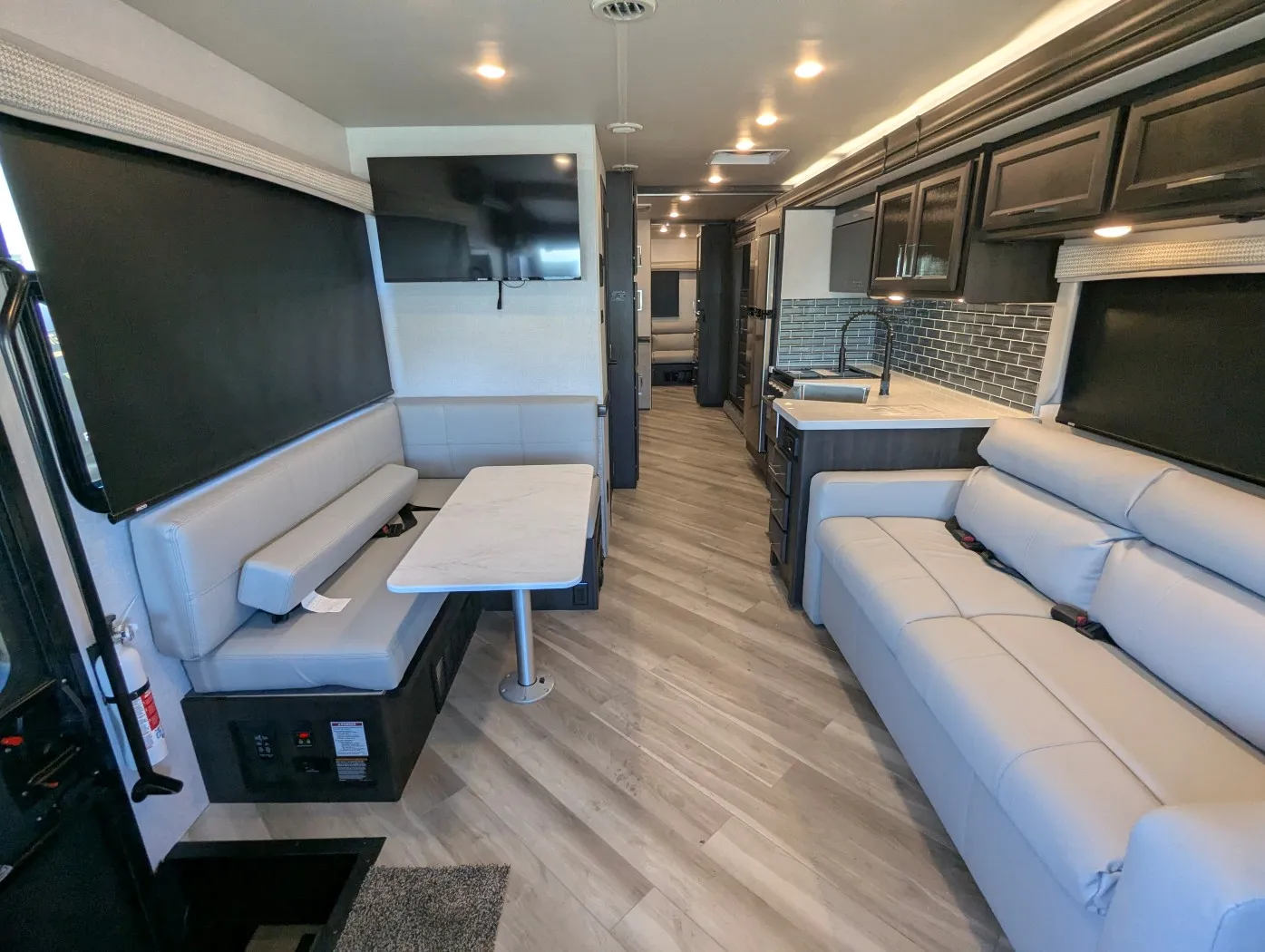 2026 Holiday Rambler Invicta 36Y — Wide motorhome interior view showing opposing lounge seating, a dinette, television, and kitchen sink with cabinetry
