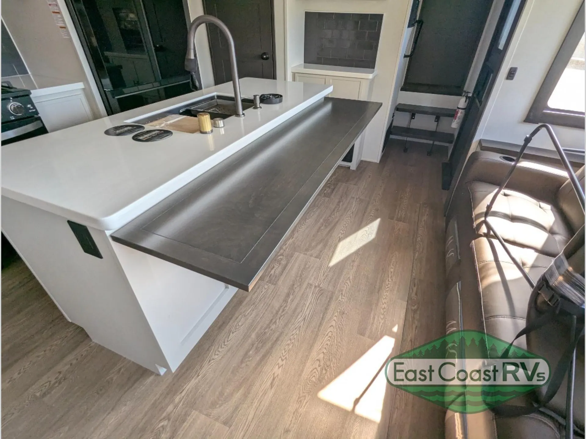 2027 Forest River Sanibel 40BUNK — Kitchen island with sink and counter seating beside a visible living room recliner and open interior walkway