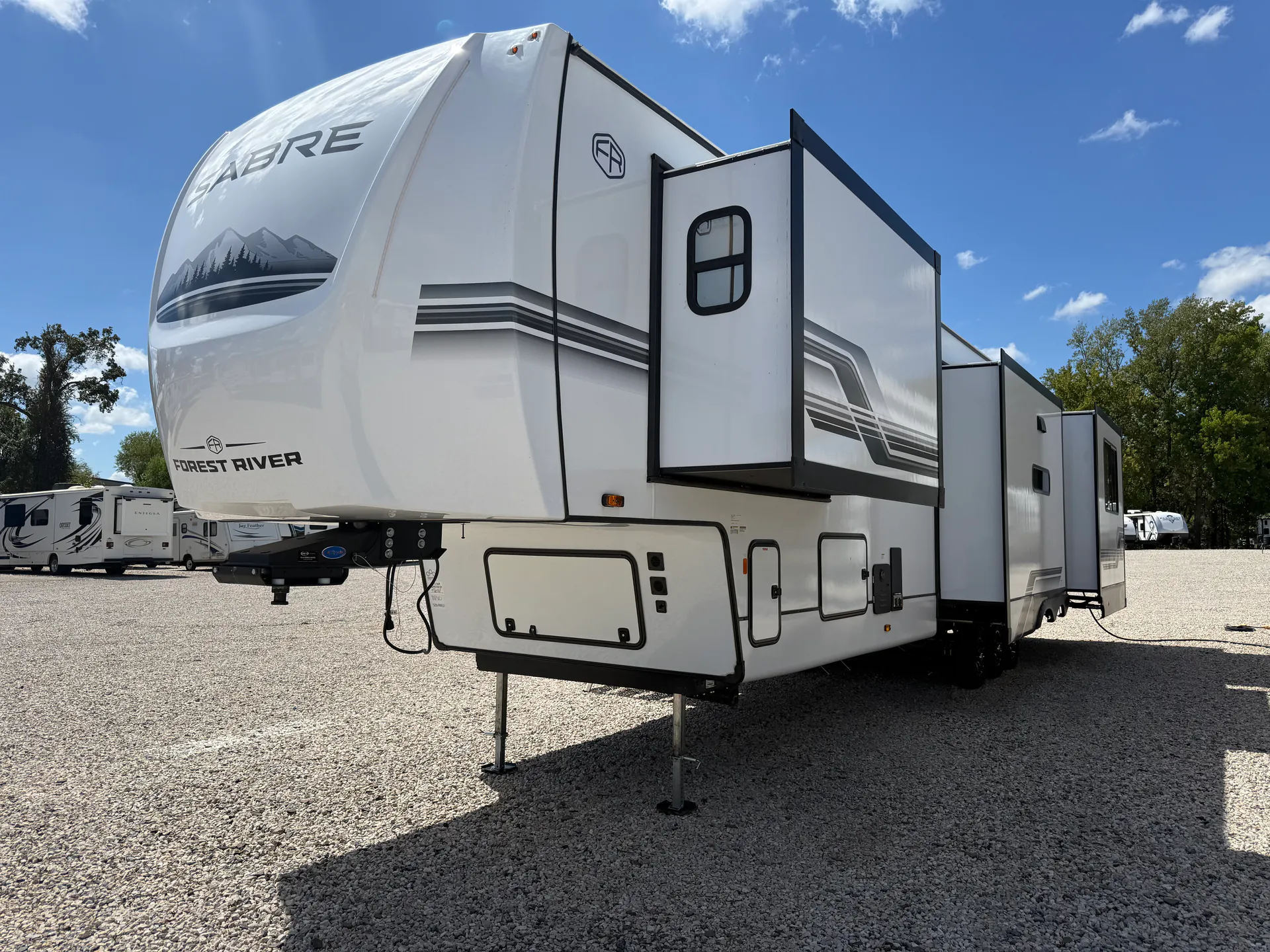 2027 Forest River Sabre 38RVHUNTER — Exterior three-quarter photograph visibly shows multiple exterior storage-compartment doors beneath the RV body and slide-outs