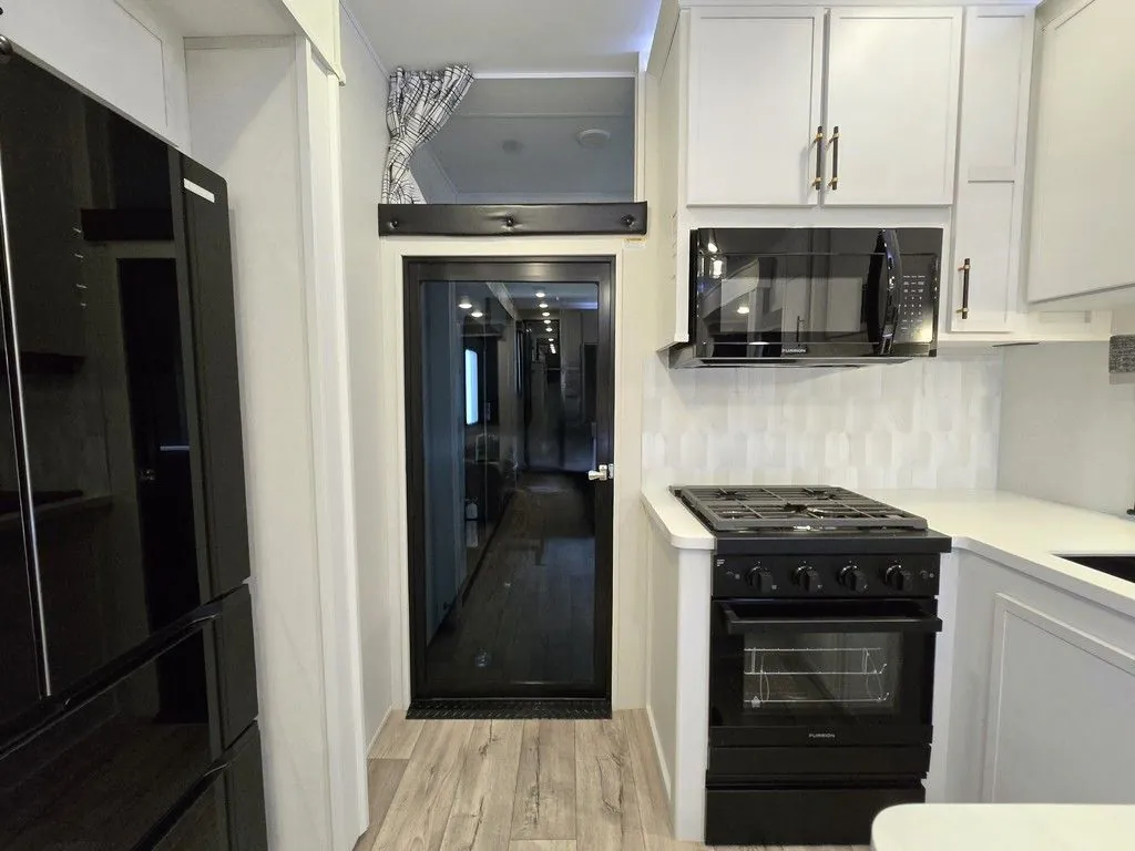 2025 Dutchmen Voltage 4225 — Fifth-wheel kitchen with refrigerator, microwave, range, oven, countertop, backsplash, and surrounding cabinetry