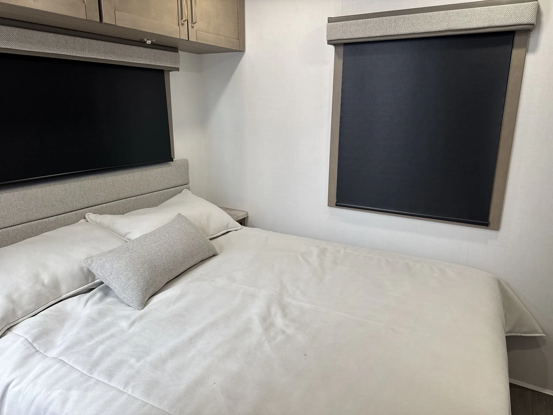 2027 Jayco Alante 29F — Main bedroom with a made bed, upholstered headboard, overhead cabinets, bedside surface, and two covered windows