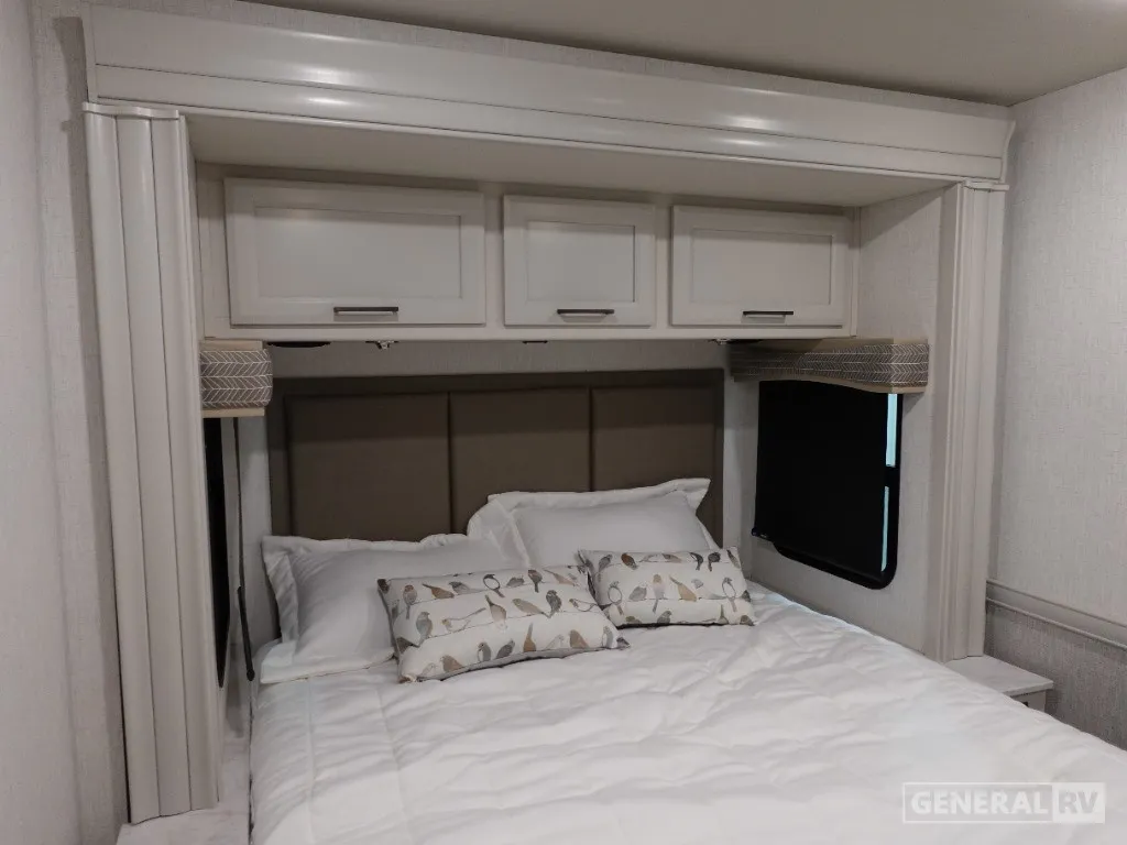 2026 Holiday Rambler Invicta 36Y — Main bedroom bed with pillows, upholstered headboard, overhead cabinets, side windows, and bedside surfaces
