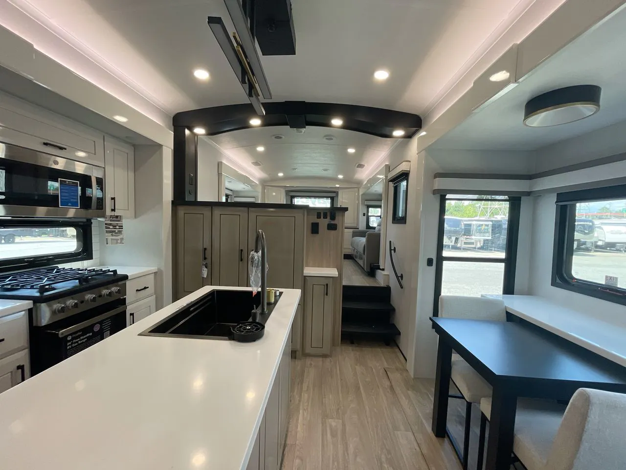 2027 Jayco Pinnacle 39FLOK — Kitchen island and range face a dining table, with stairs and lounge seating visible beyond the central cabinetry