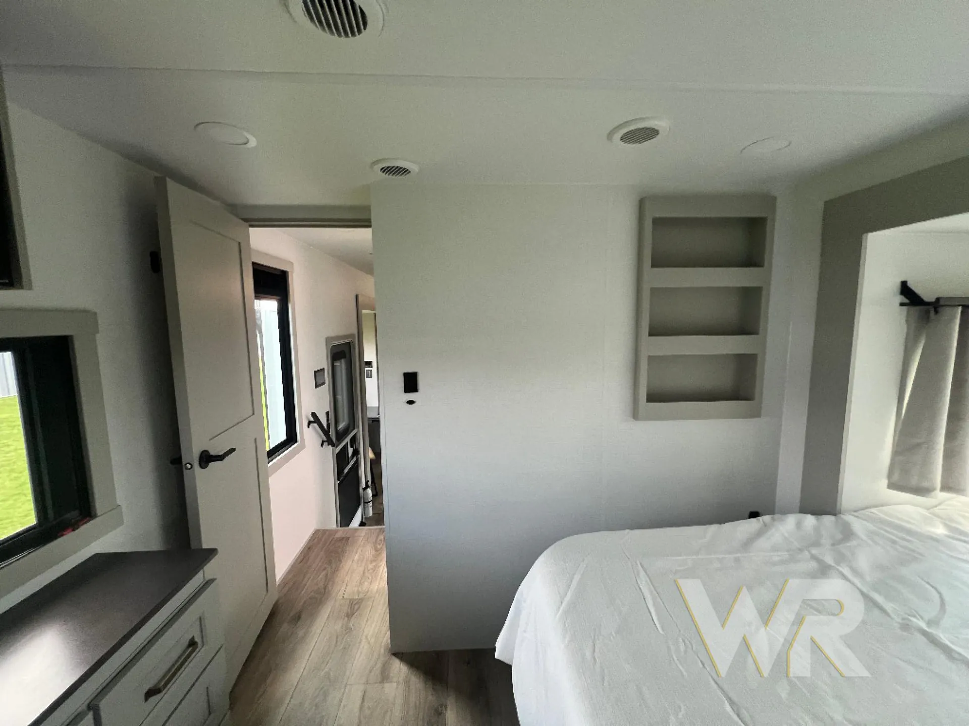 2026 Brinkley Model G 3950 — Main bedroom with bed and dresser opening toward the hallway and visible kitchen cabinetry