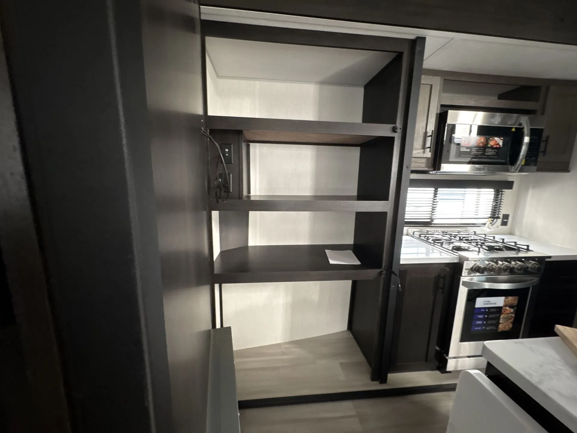2026 Forest River Cherokee Wolf Pack 397STAY — Travel trailer kitchen pantry cabinet open beside a microwave, range, counter, and upper cabinets