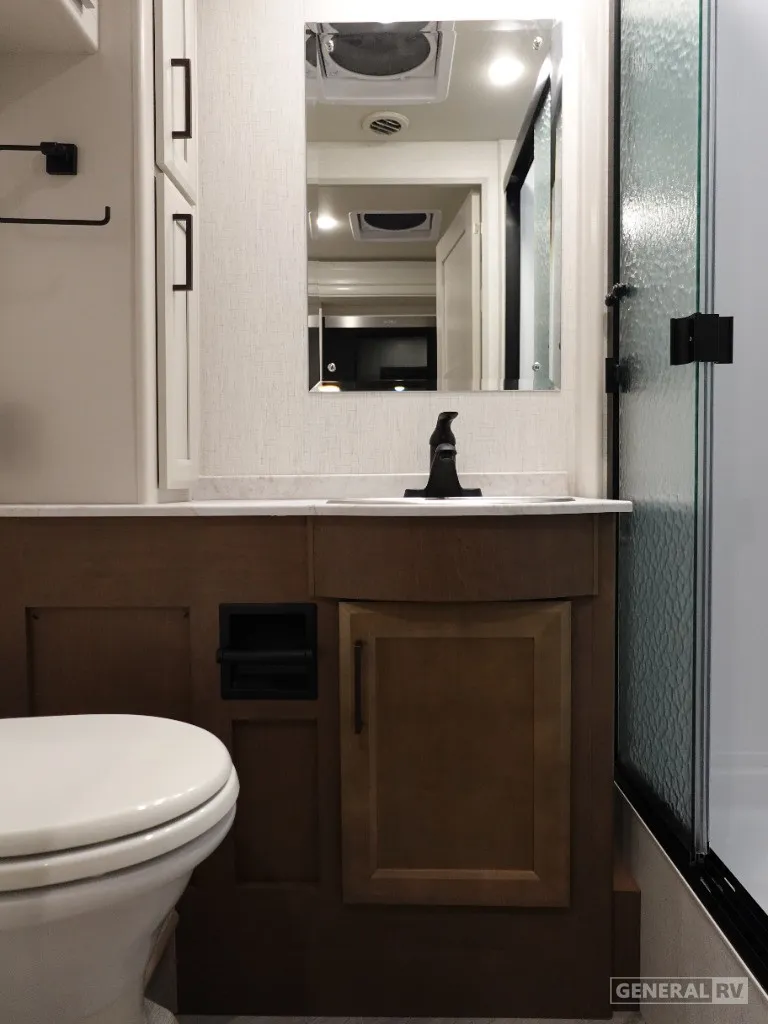 2026 Holiday Rambler Invicta 36Y — Bathroom vanity with sink, mirror, wood cabinetry, toilet, and textured glass shower door
