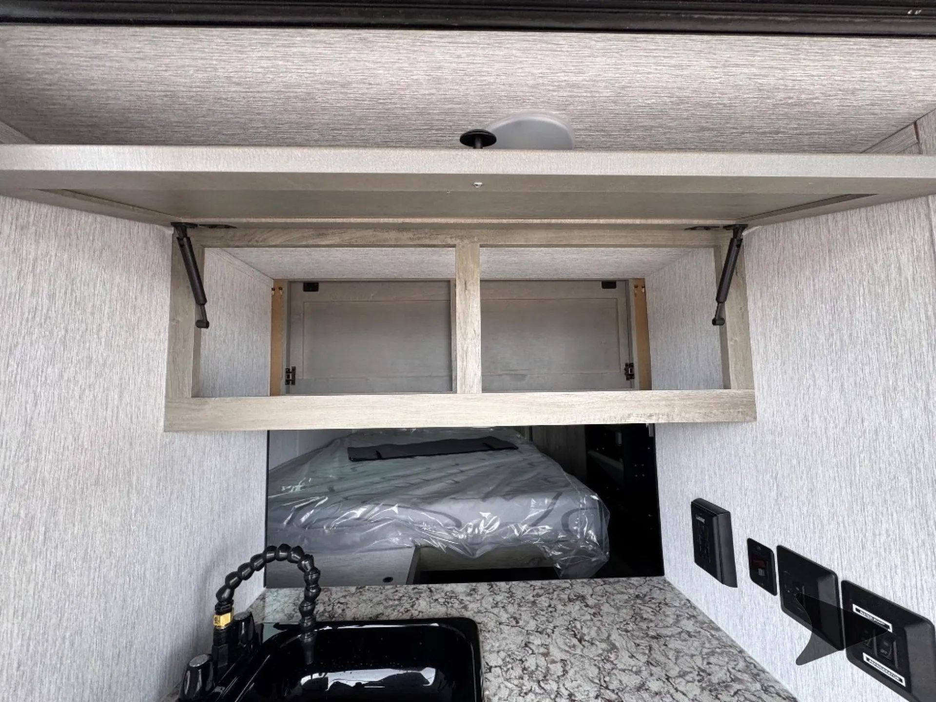 2026 Wayfinder GO LITE LTD Solo — Travel trailer kitchen counter and sink face a sleeping bed, with overhead cabinets and wall controls visible