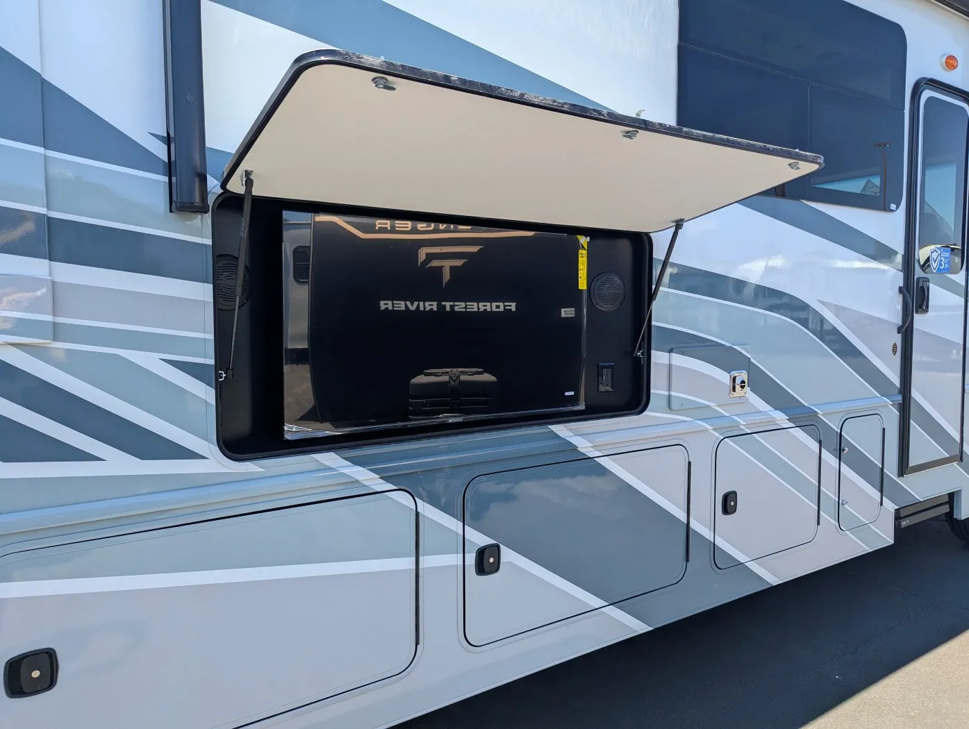 2026 Holiday Rambler Invicta 36Y — Open exterior side compartment visibly shows an installed entertainment television and surrounding exterior storage area