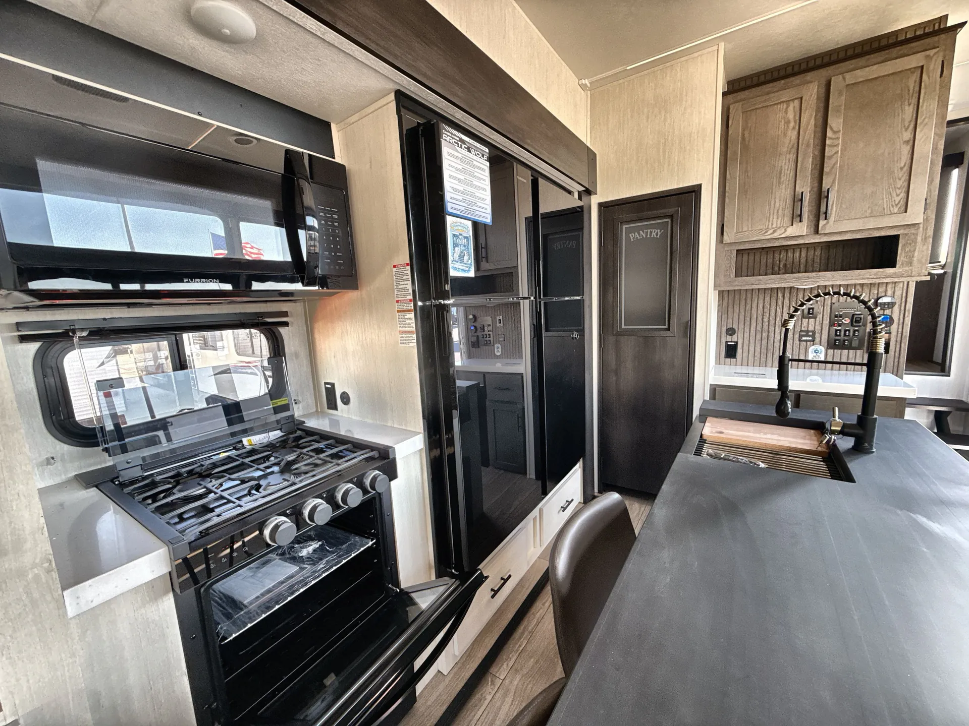 2026 Forest River Arctic Wolf 38LEAH.G — Fifth wheel kitchen with range, microwave, refrigerator, sink, pantry, cabinetry, and adjacent dining counter
