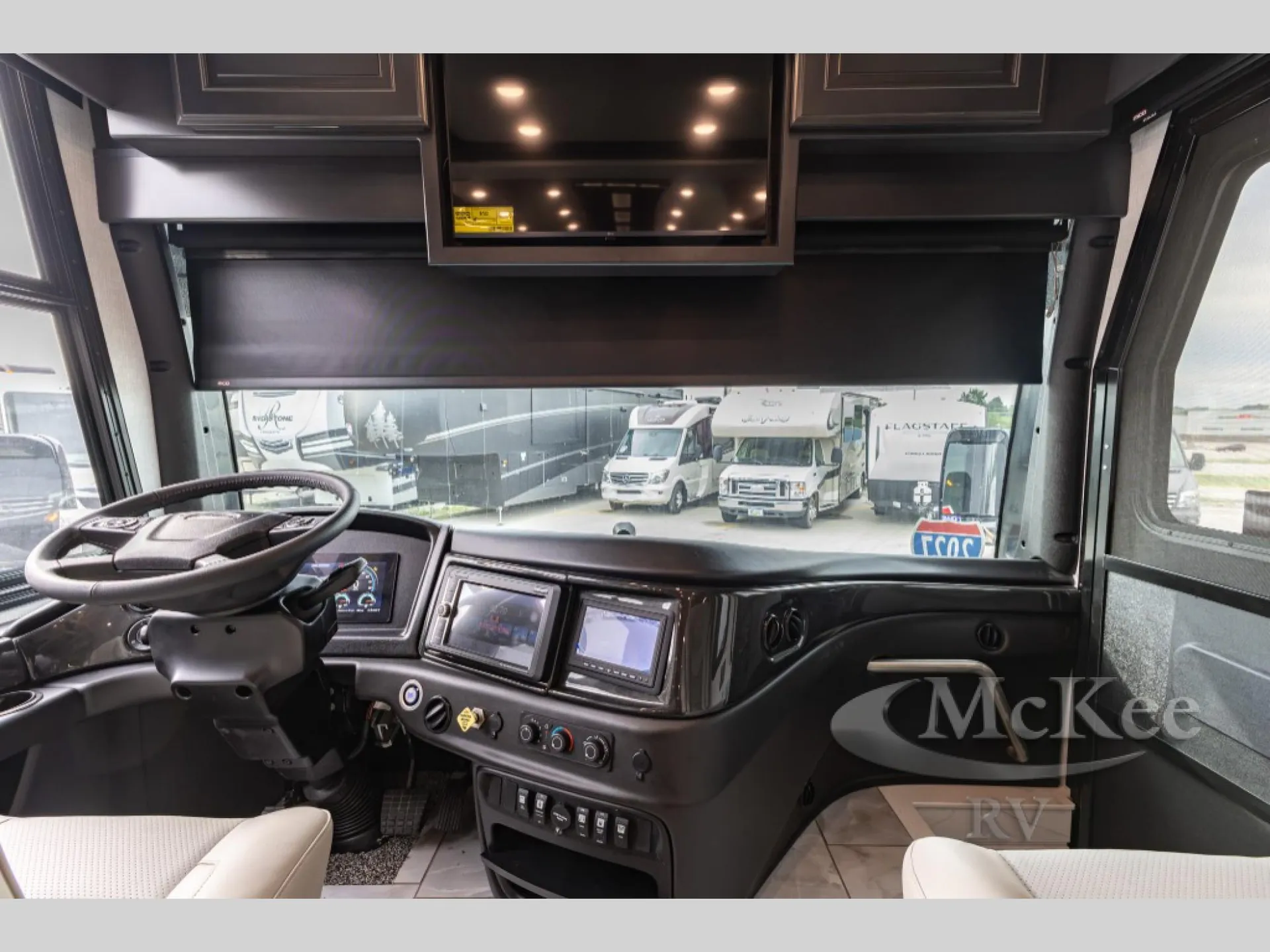 2027 Fleetwood Discovery LXE 40M — Class A motorhome cockpit with steering wheel, dashboard screens, climate controls, switches, passenger seat, and windshield