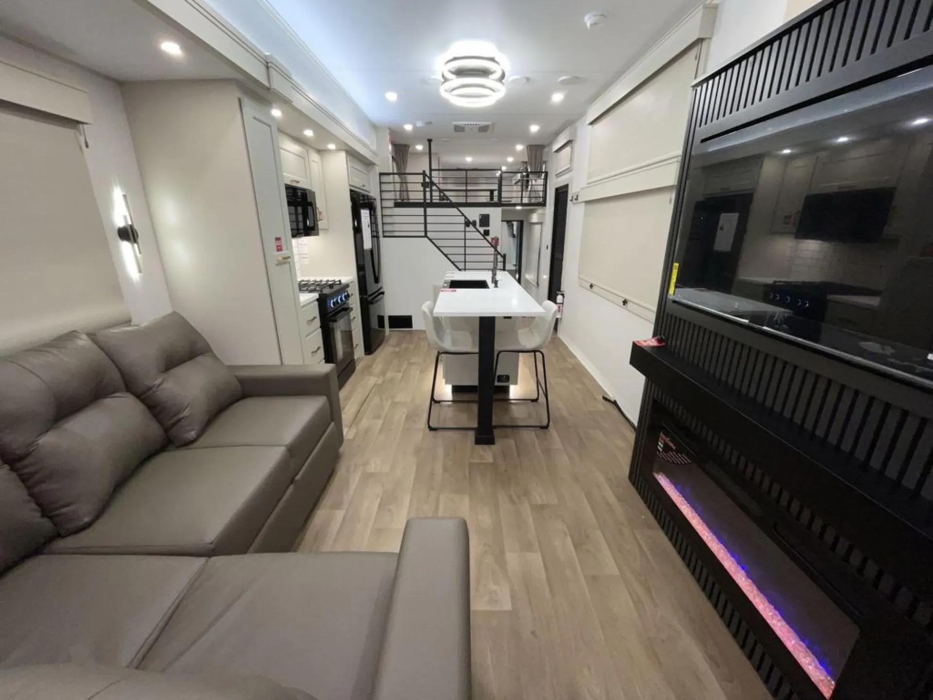 2026 Grand Design Foundation 42GD — Destination trailer interior with a sectional sofa, dining island, kitchen appliances, fireplace, and stairs to an upper sleeping area