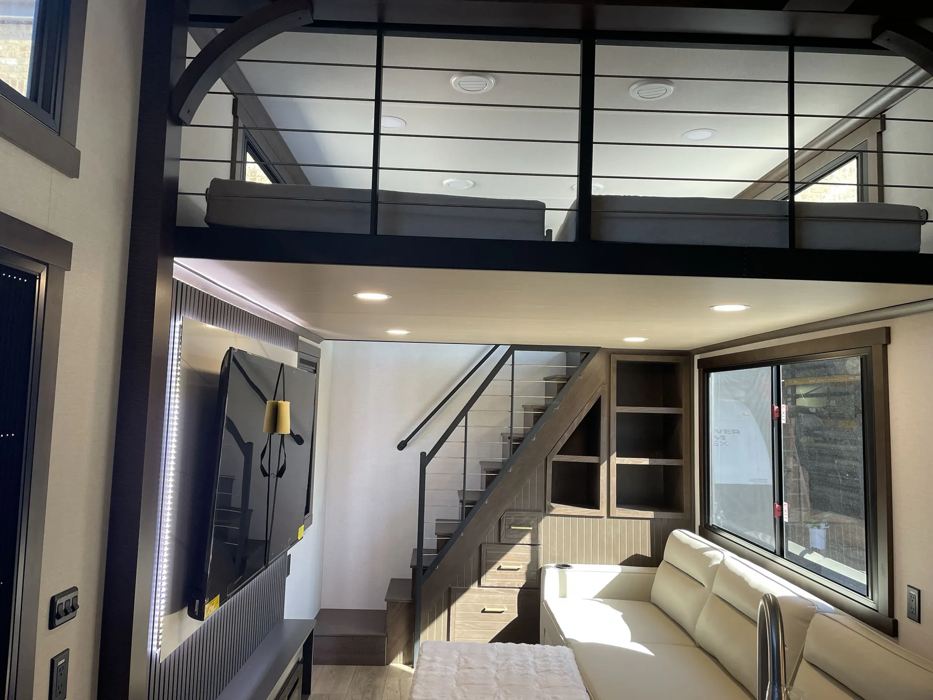 2026 Forest River Cedar Creek Cottage 41FWC — Fifth wheel loft bed above a living area with sofa, television, staircase, and built-in shelving
