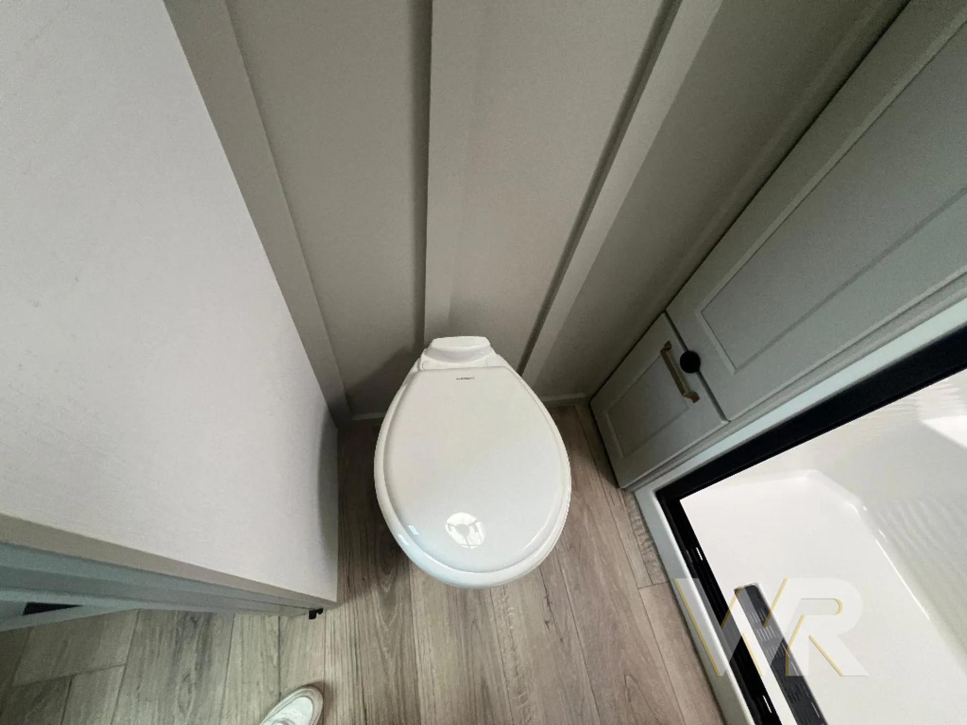2026 Brinkley Model G 3950 — Bathroom toilet beside wood-look flooring, wall cabinetry, and the edge of a shower enclosure