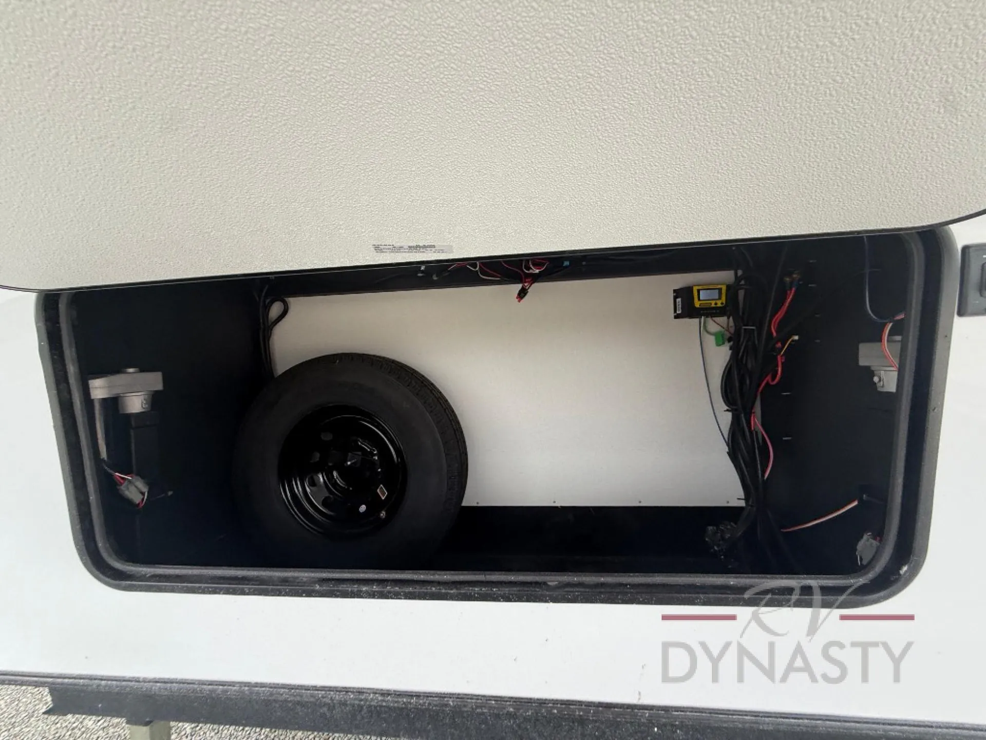 2027 Forest River Sanibel 40BUNK — Open exterior storage compartment visibly contains a spare tire and wiring/equipment