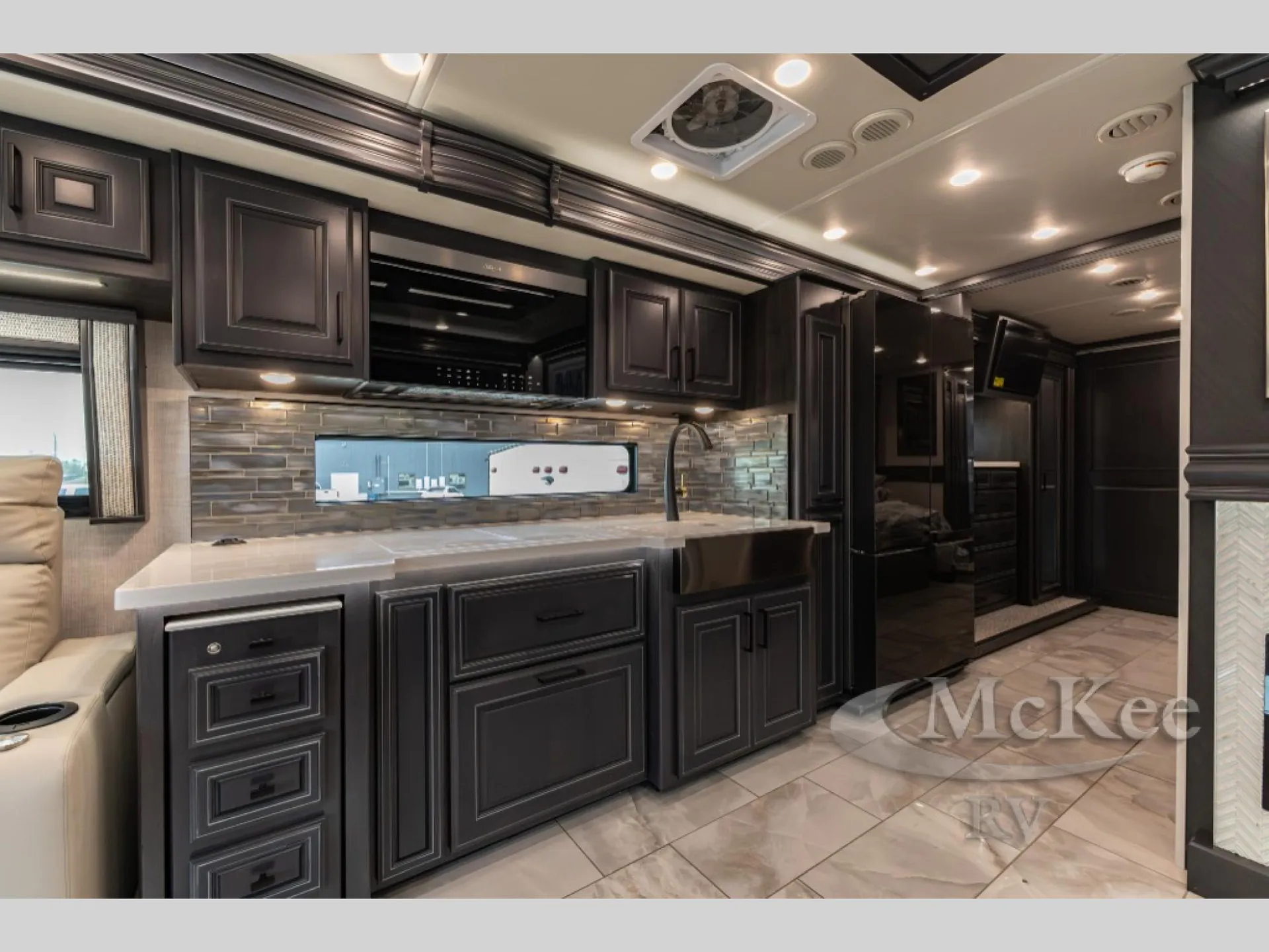 2027 Fleetwood Discovery LXE 40M — Kitchen with sink, counter, backsplash, cabinets, and refrigerator opening beside a living recliner