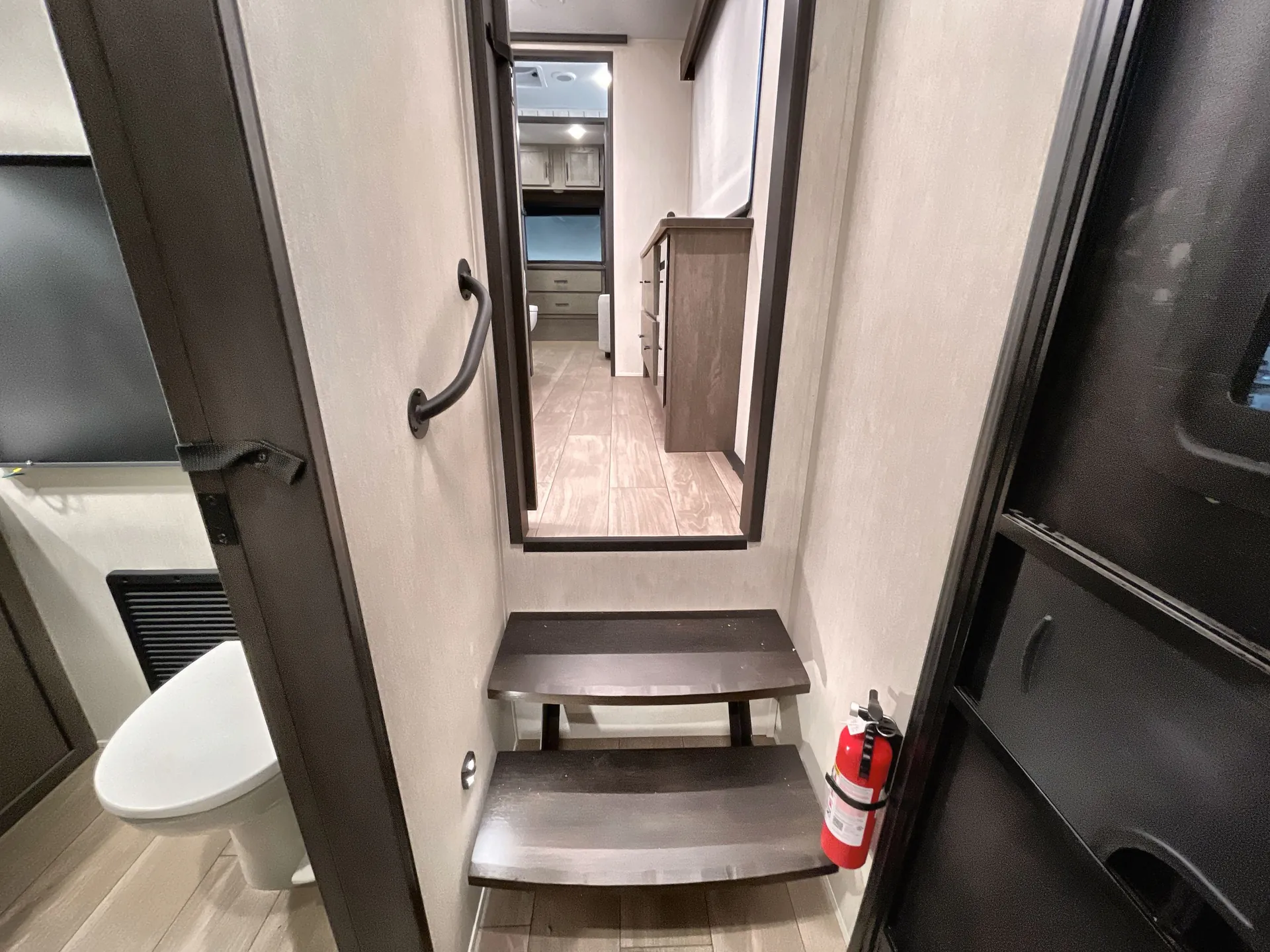 2026 Forest River Arctic Wolf 38LEAH.G — Fifth-wheel interior stairway with handrail and fire extinguisher leading from the bathroom toward upper living spaces