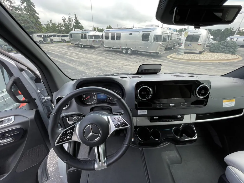 2026 Airstream Atlas Murphy Suite — Driver cockpit viewed from the seat with steering wheel, gauges, infotainment screen, dashboard controls, and cupholders