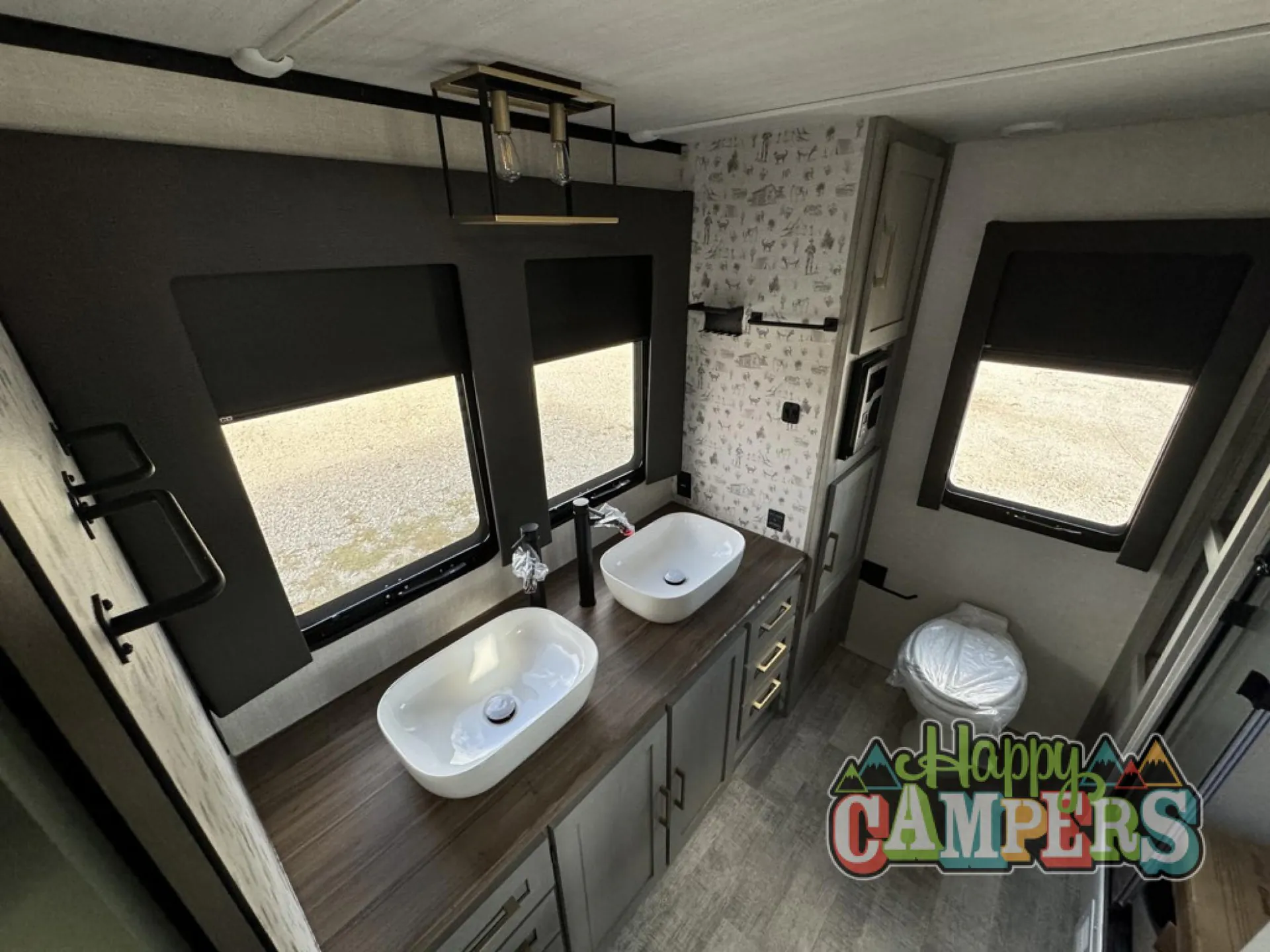 2025 Forest River IBEX RVS3 — Travel trailer bathroom vanity with two vessel sinks, storage drawers, windows, and an adjacent toilet