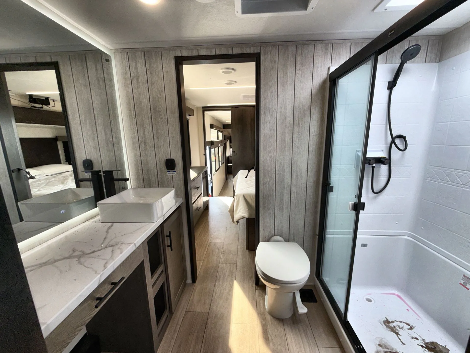 2026 Forest River Arctic Wolf 38LEAH.G — Bathroom overview with vanity, vessel sink, toilet, glass shower, and centered doorway toward the bedroom