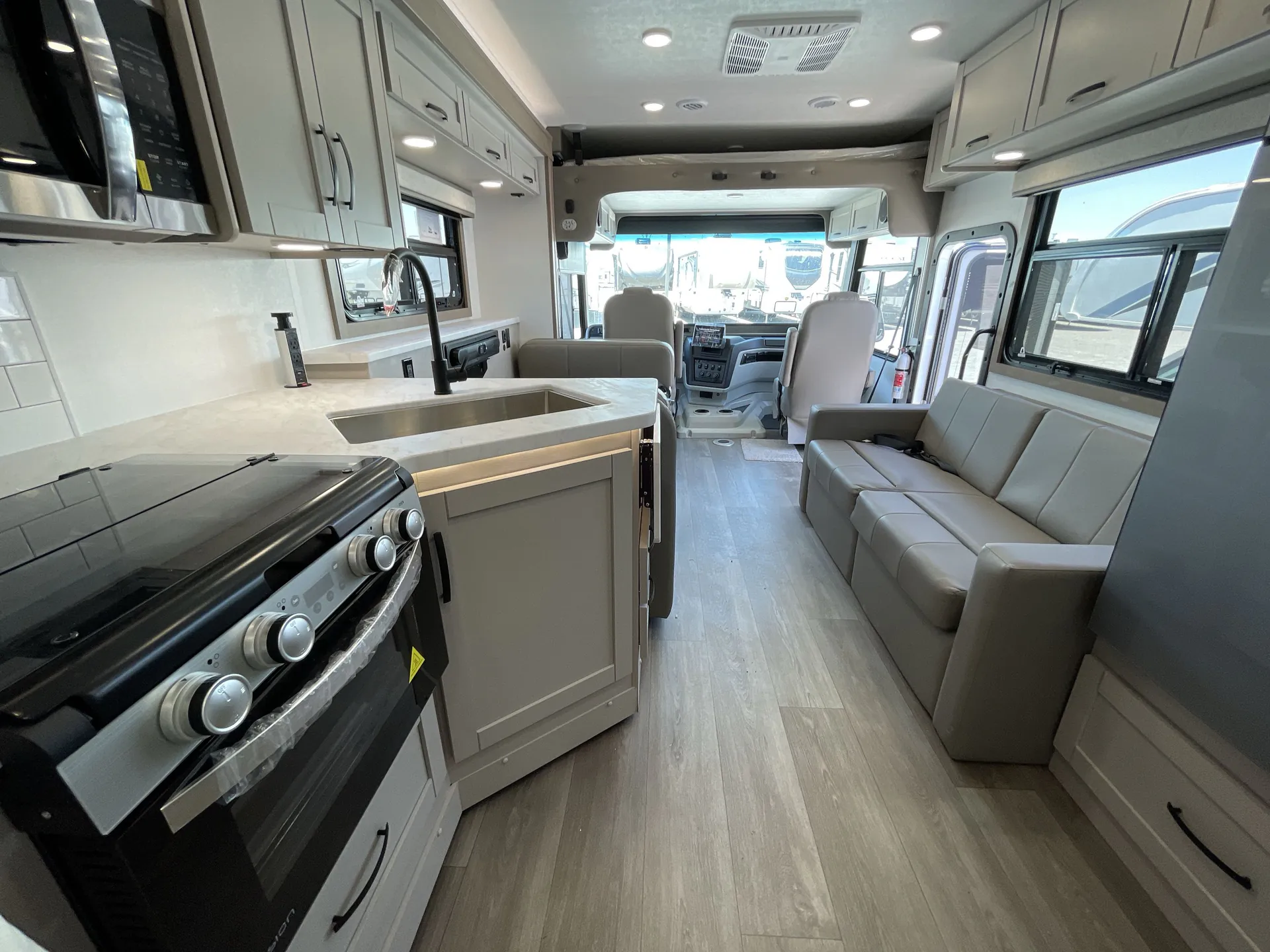 2027 Jayco Alante 29F — Kitchen island with sink and range facing a sofa and open motorhome cockpit