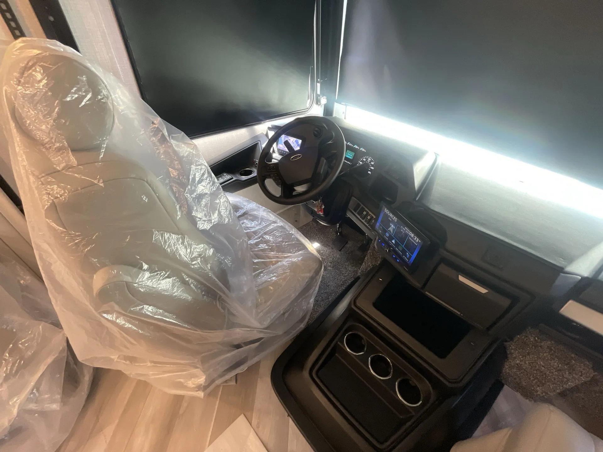 2026 Holiday Rambler Invicta 36Y — Angled cockpit view showing the covered driver’s seat, steering wheel, instrument cluster, infotainment screen, and center console