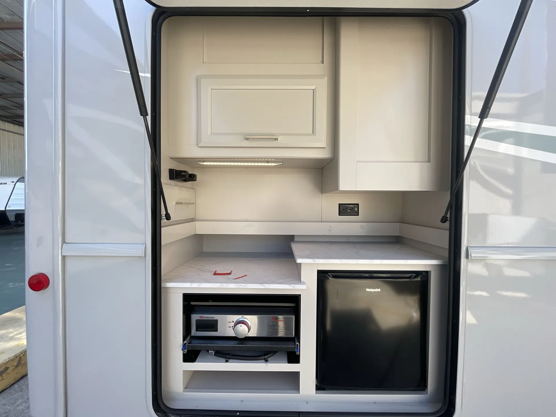 2026 Holiday Rambler Invicta 36Y — Exterior hatch visibly contains an installed refrigerator, grill, countertop, cabinets, and electrical outlet, forming an outdoor kitchen
