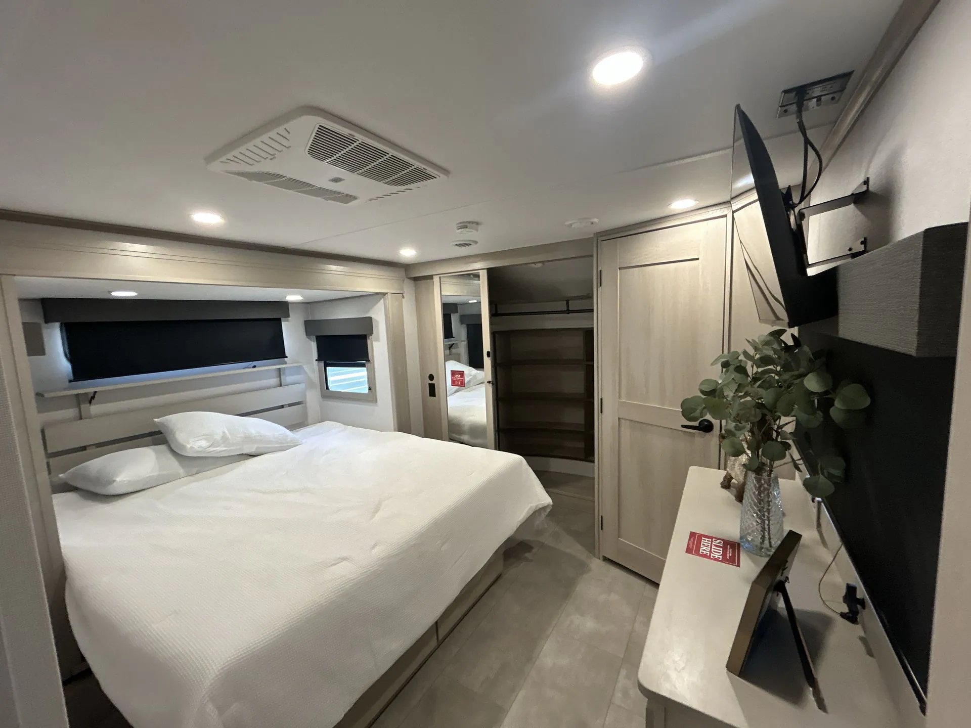 2026 Grand Design Solitude 391DL — Main bedroom with made bed, overhead television, dresser, wardrobe, and closet shelving