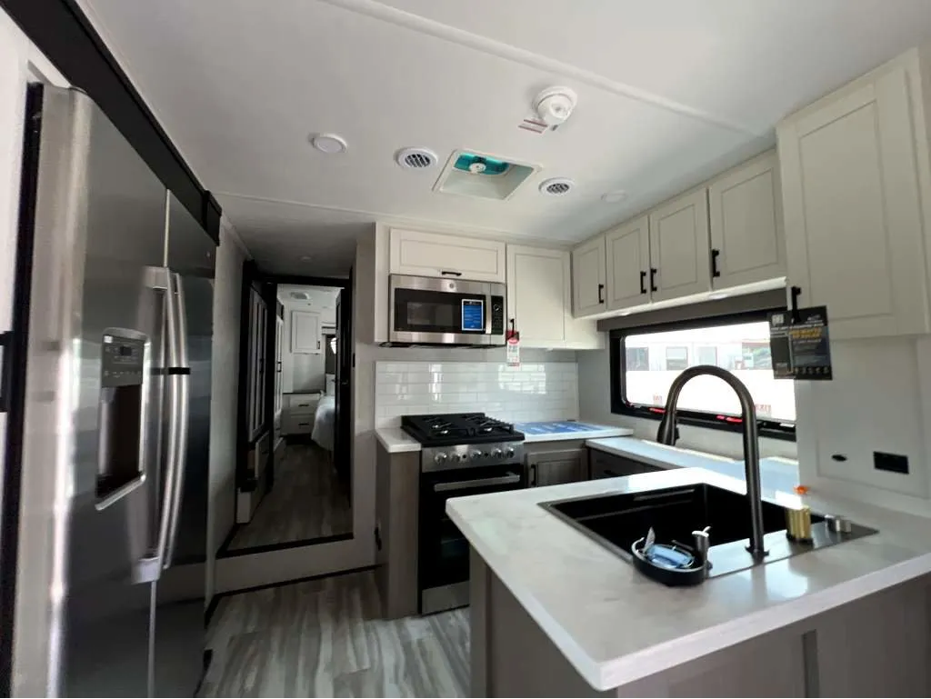 2025 Jayco Seismic Luxury Series 4113 — Fifth-wheel kitchen with refrigerator, microwave, range, sink, island counter, and overhead cabinets
