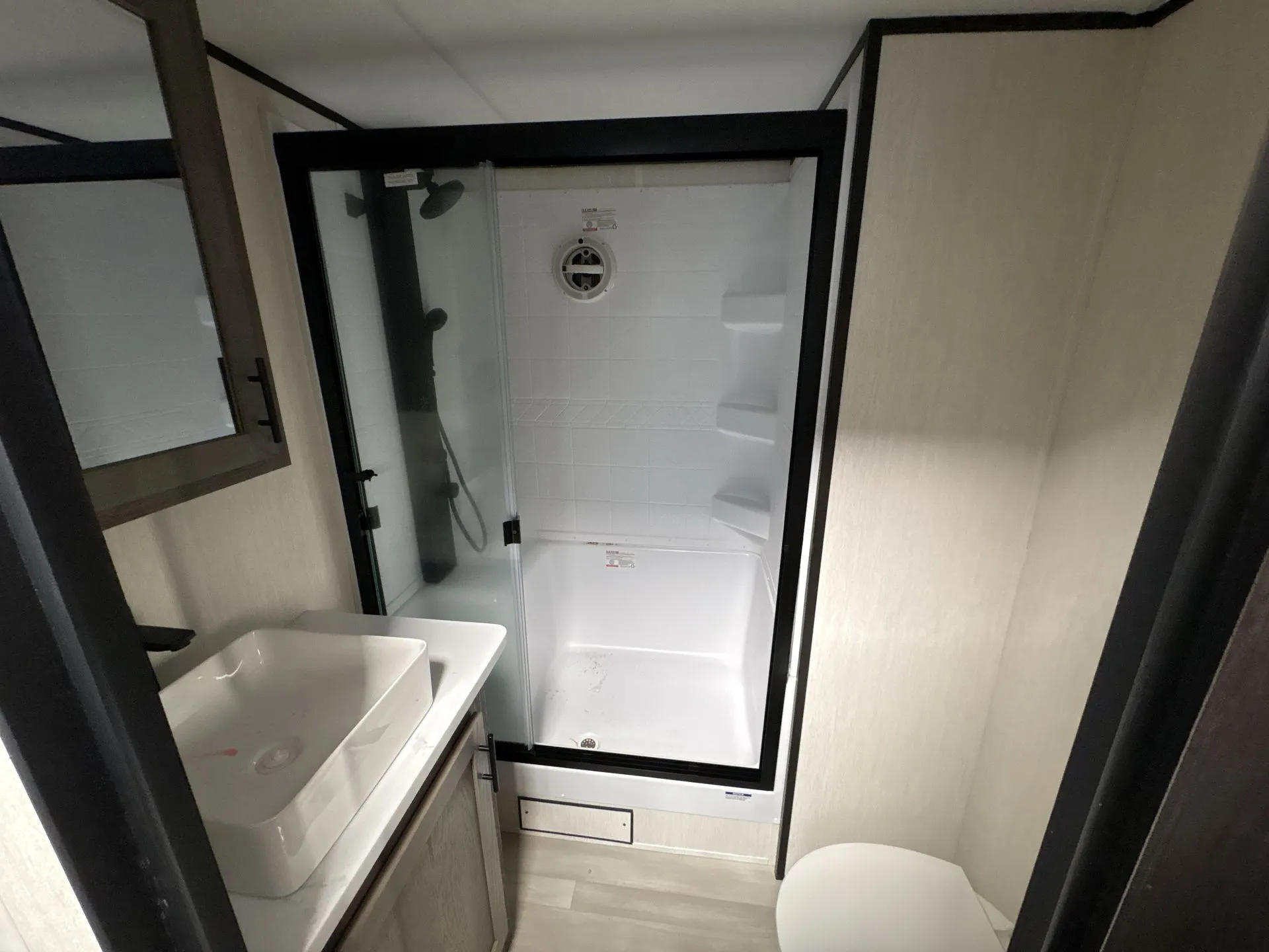 2026 Forest River Cherokee Wolf Pack 397STAY — Bathroom contains a glass-enclosed shower, corner shelves, vessel sink, mirrored cabinet, and toilet