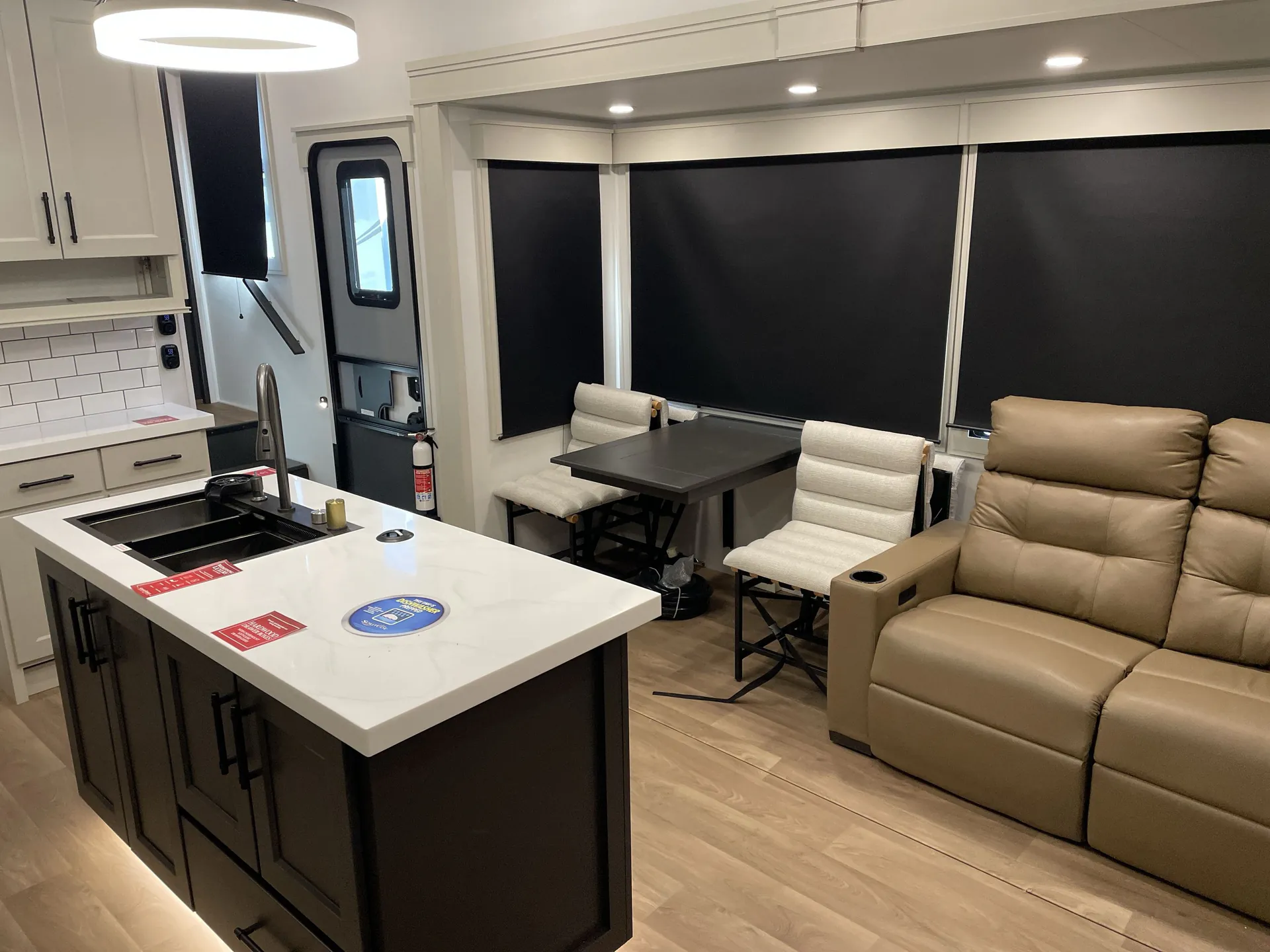 2026 Grand Design Solitude 391DL — Fifth-wheel living area with theater sofa, freestanding dining table, chairs, and kitchen island
