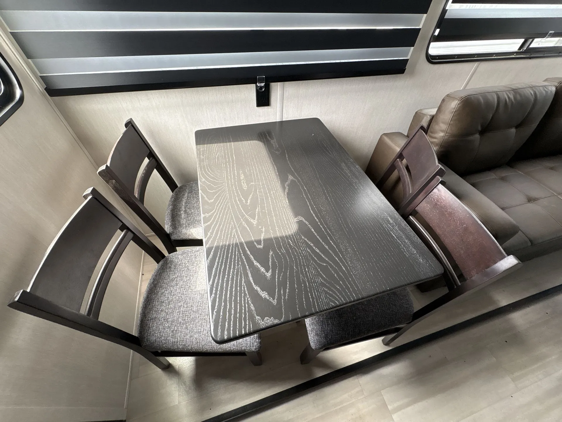 2026 Forest River Cherokee Wolf Pack 397STAY — Travel trailer dinette with four chairs, a dark tabletop, and a nearby upholstered recliner