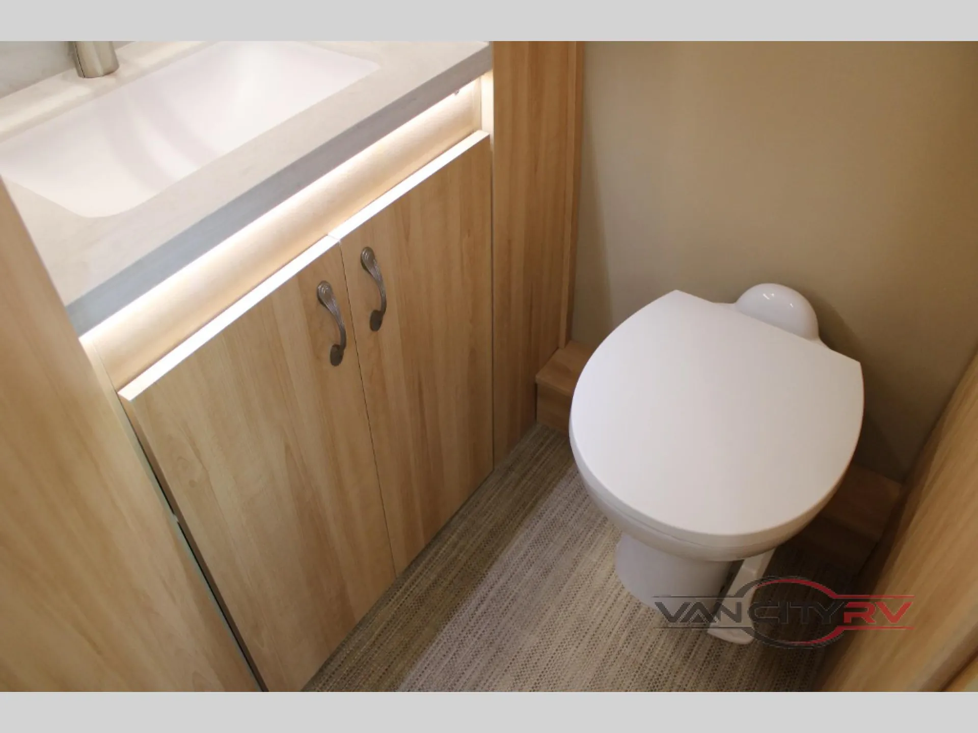 2024 Chinook RV Maverick SS — Compact bathroom with toilet, white countertop, wood vanity cabinets, and illuminated trim