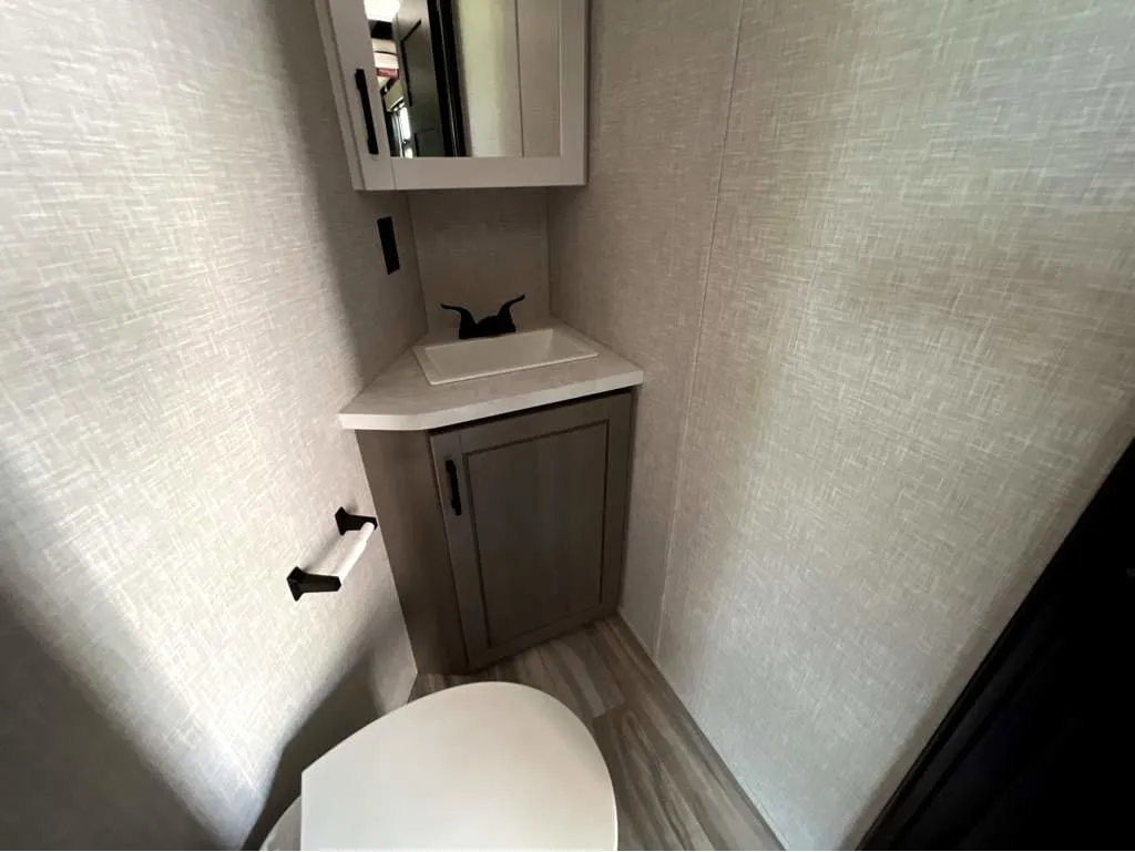 2025 Jayco Seismic Luxury Series 4113 — Compact bathroom with toilet, vanity cabinet, countertop sink, mirror, and toilet-paper holder