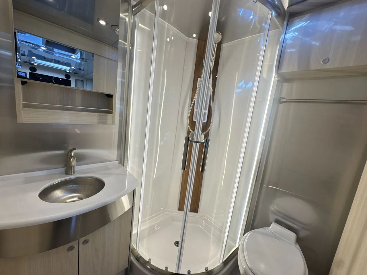 2026 Airstream Atlas Murphy Suite — Compact bathroom with corner glass shower, round sink vanity, mirror, and toilet