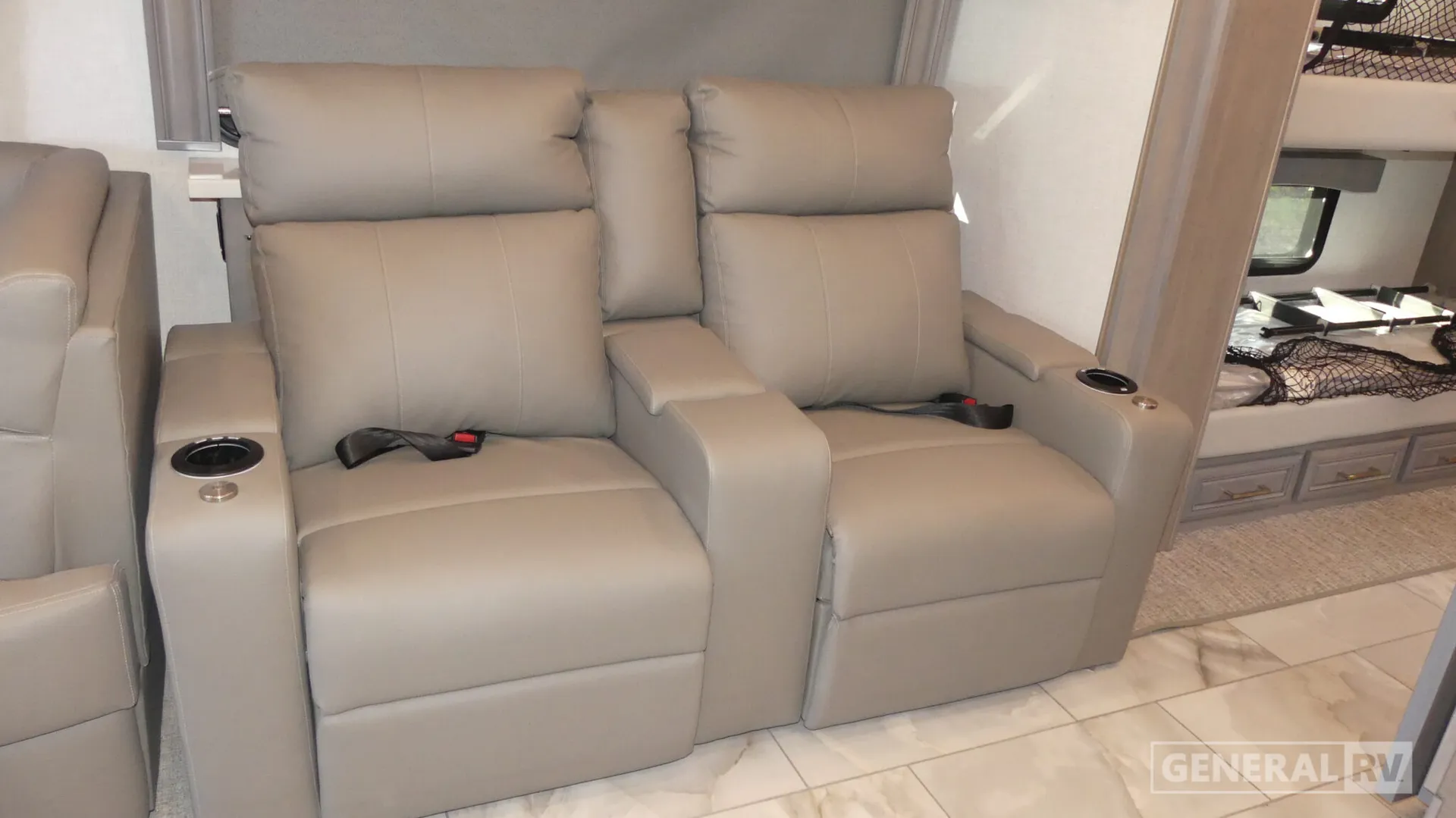 2026 Fleetwood Discovery LXE 40G — Two reclining lounge seats beside a sofa edge, with a visible bed and drawers through the adjacent opening