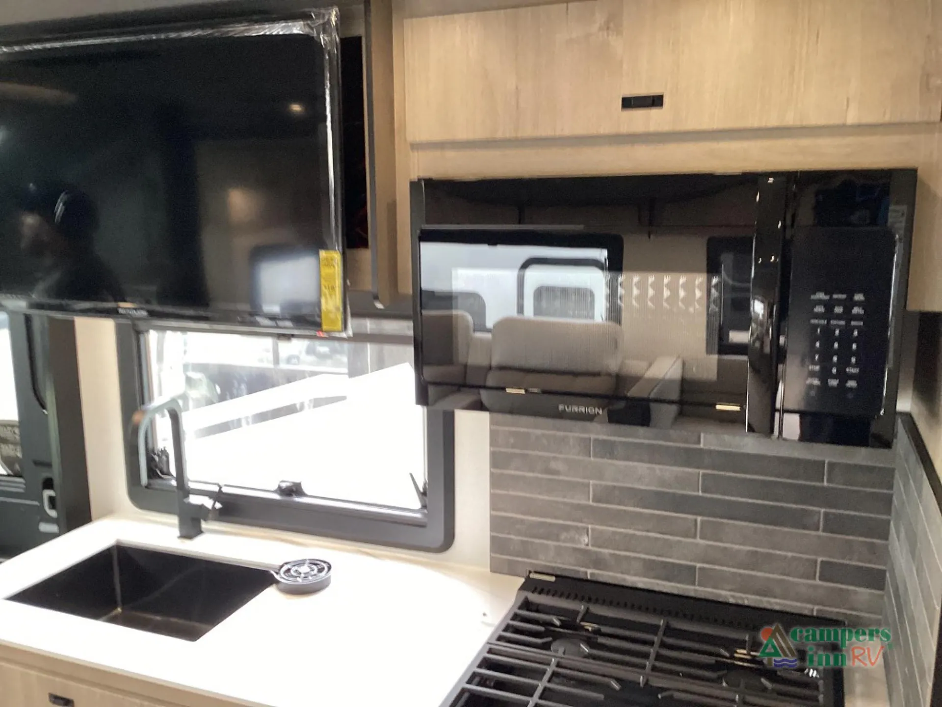 2027 Grand Design Lineage Series F 31ZW — Kitchen counter with sink, gas cooktop, microwave, backsplash, window, and wall-mounted television