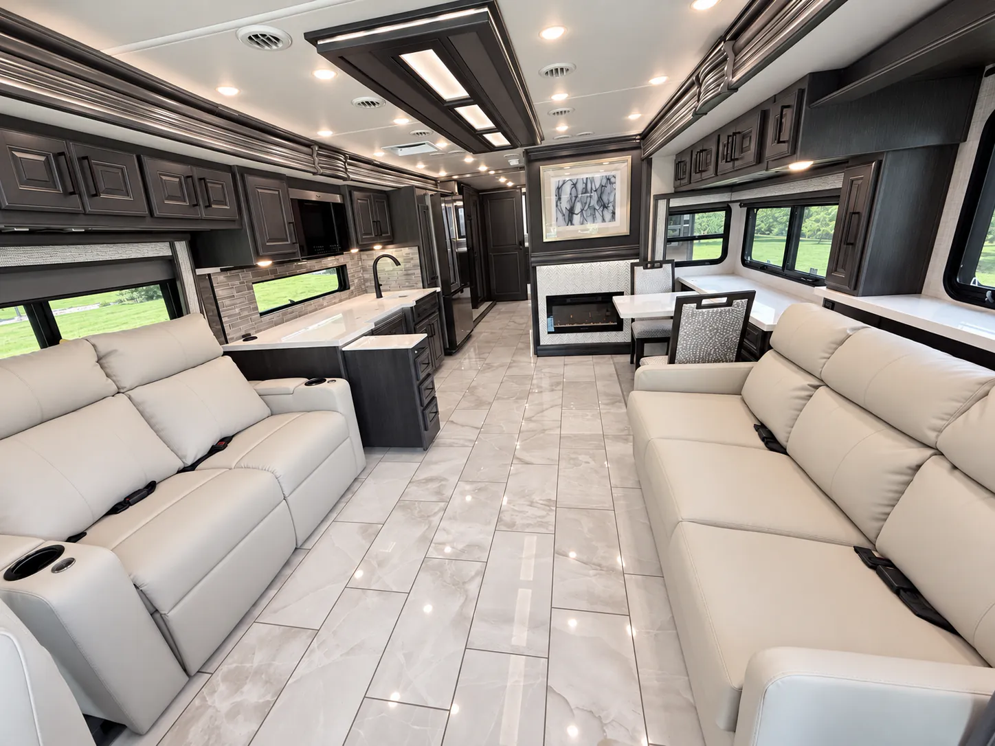 2027 Fleetwood Discovery LXE 40M — Class A lounge with opposing sofas, adjacent kitchen counter and sink, and dinette around a central aisle