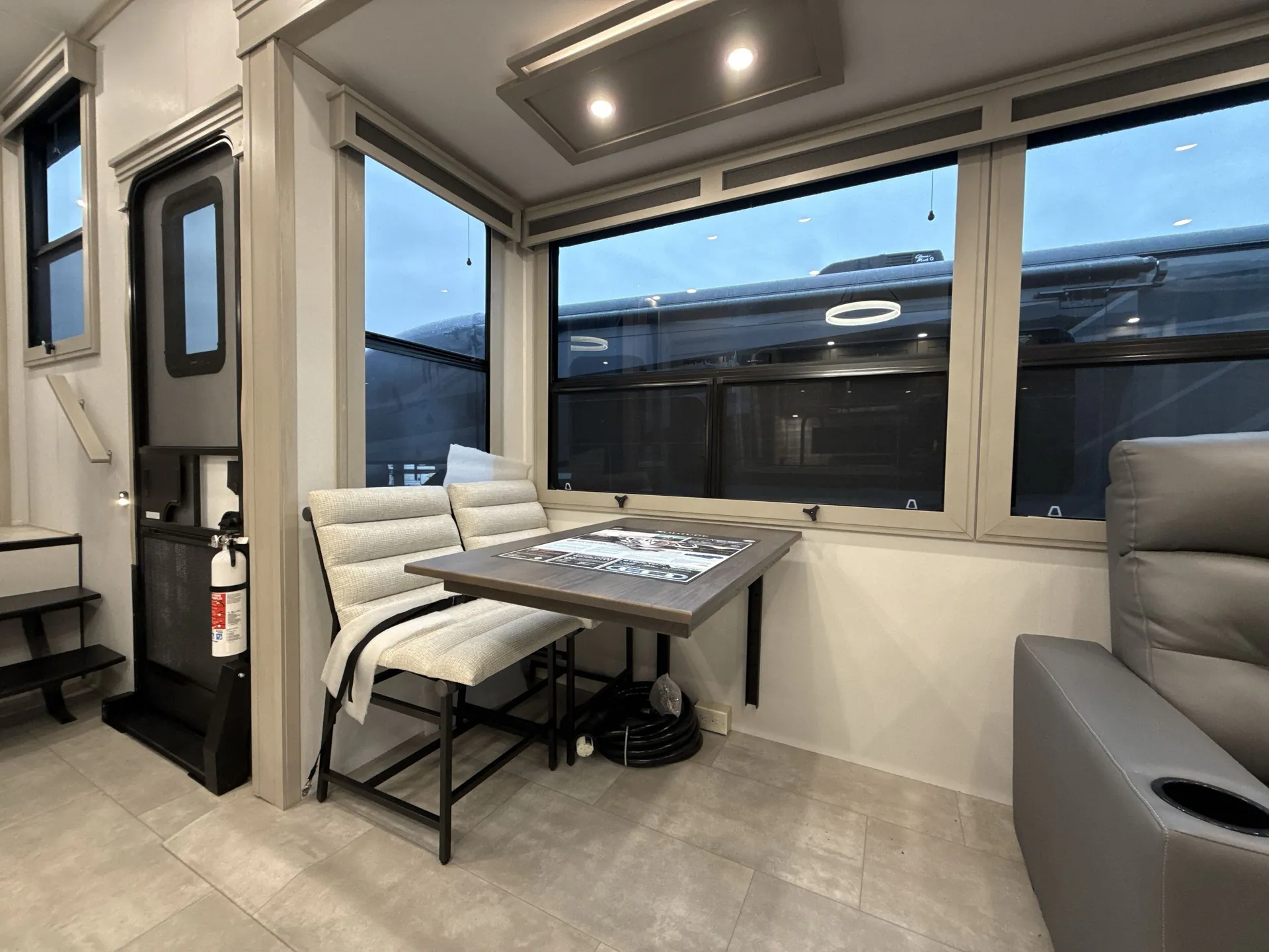 2026 Grand Design Solitude 391DL — Dinette table and chairs beside a theater recliner in a windowed RV living area