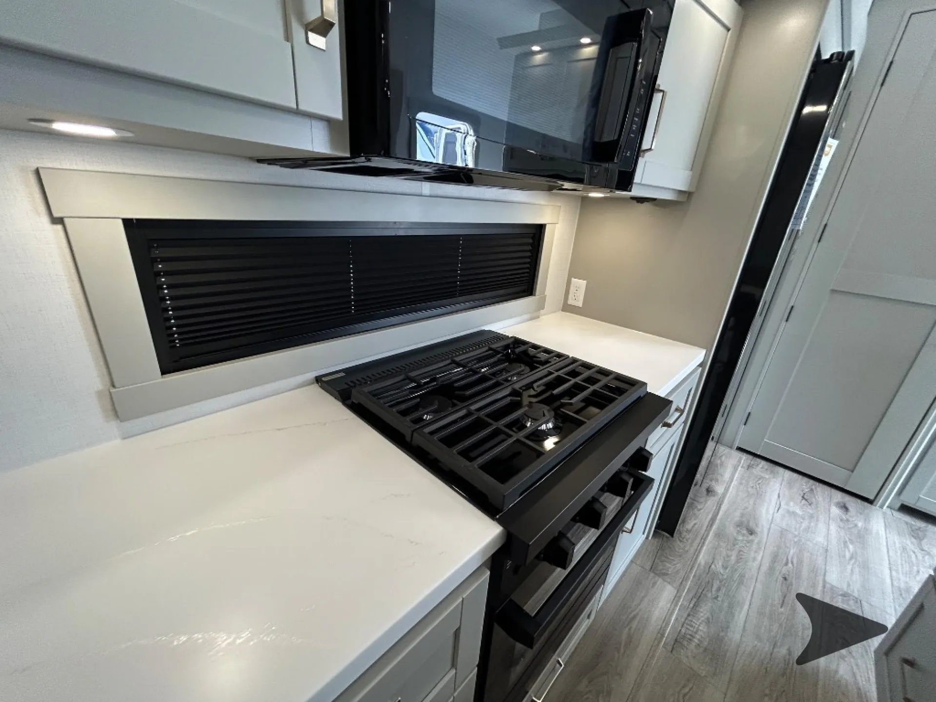 2026 Brinkley Model Z 3515 — Fifth-wheel kitchen cooktop and oven beside a broad countertop, upper microwave, refrigerator edge, and hallway