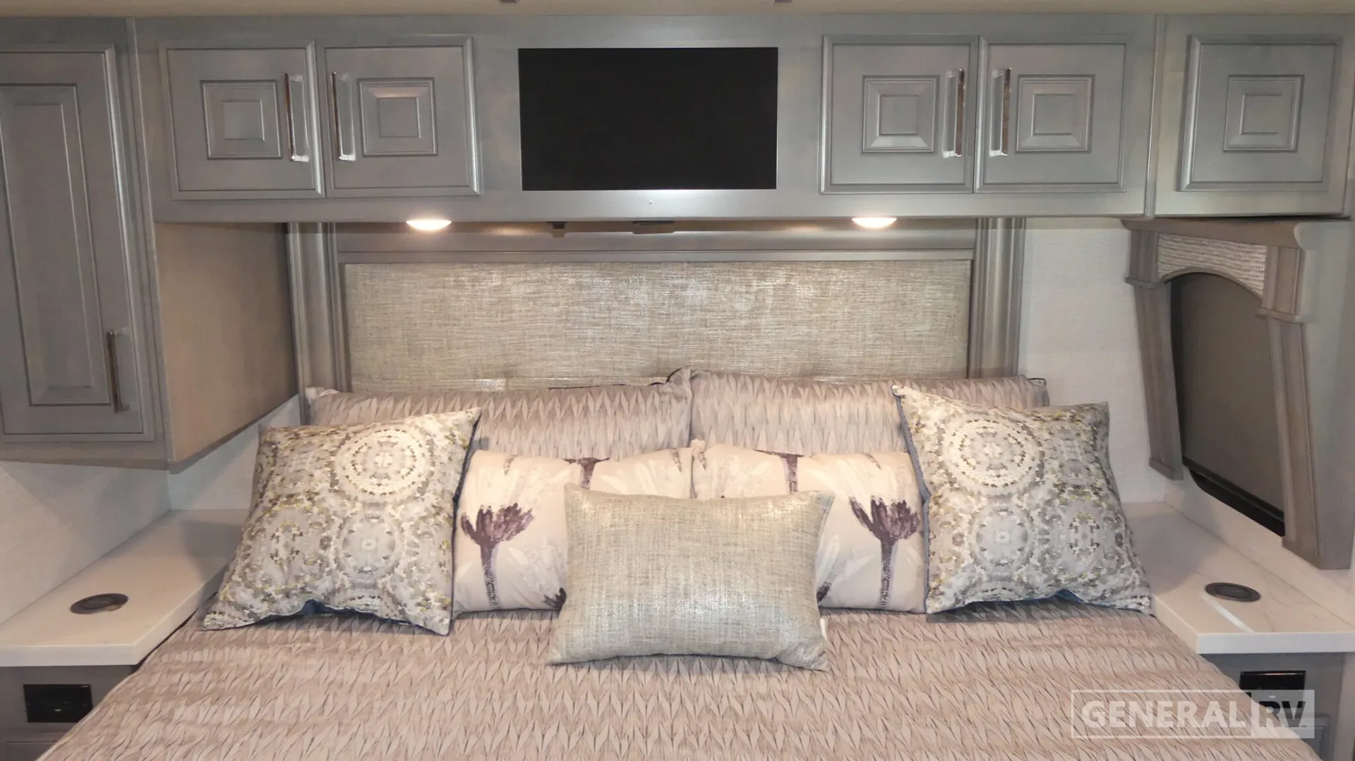 2026 Fleetwood Discovery LXE 40G — Bedroom bed with pillows, overhead cabinets, side nightstands, and a wall-mounted television