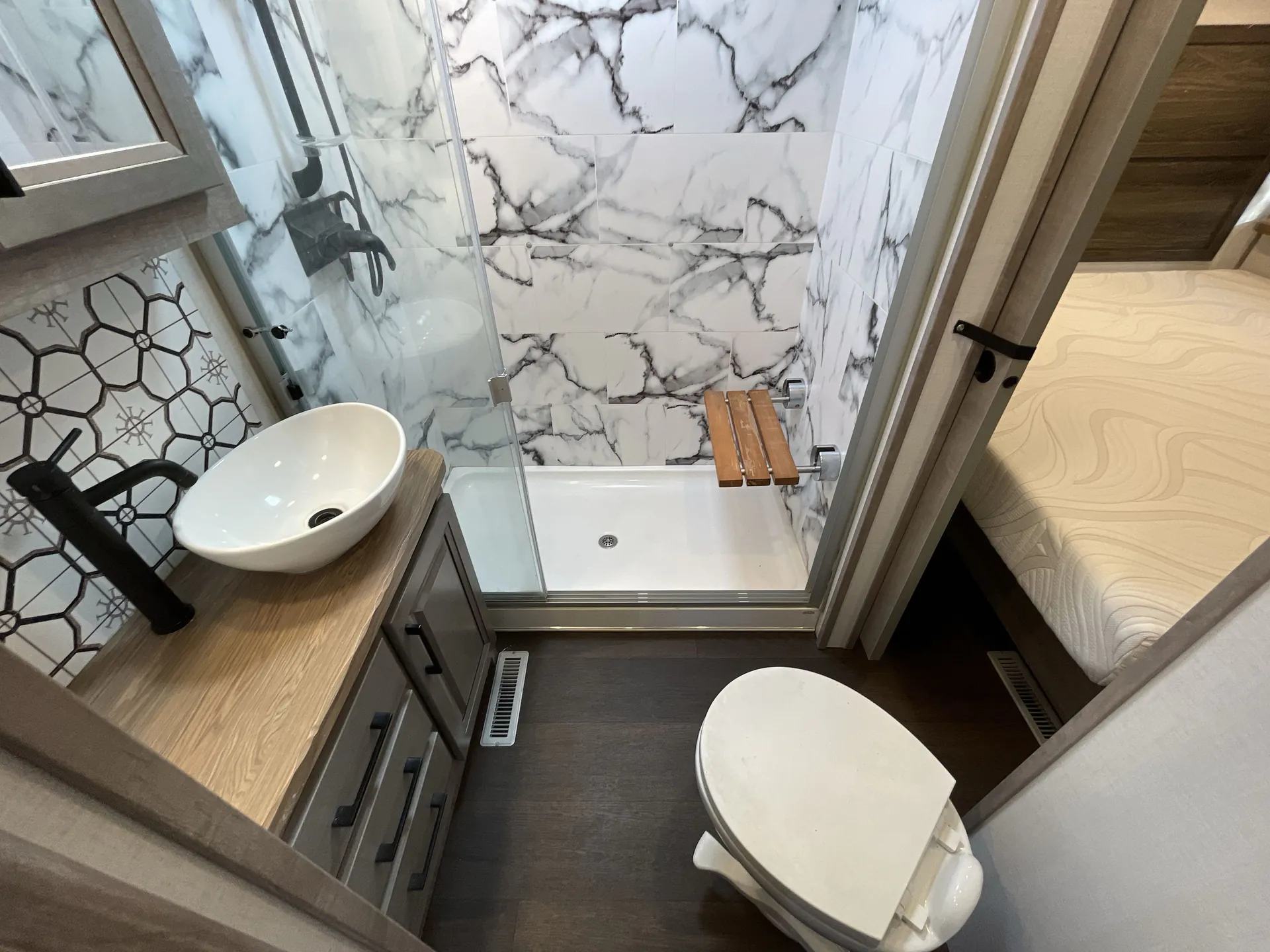 2023 Dutchmen Voltage 4225 — Bathroom interior with vessel sink, toilet, glass shower enclosure, marble-pattern walls, and wooden shower seat