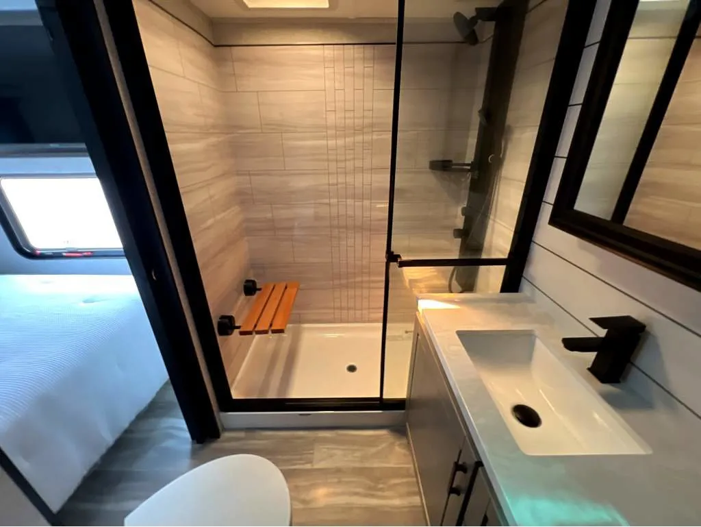 2025 Jayco Seismic Luxury Series 4113 — Bathroom showing glass shower enclosure, tiled walls, bench, toilet, and vanity sink
