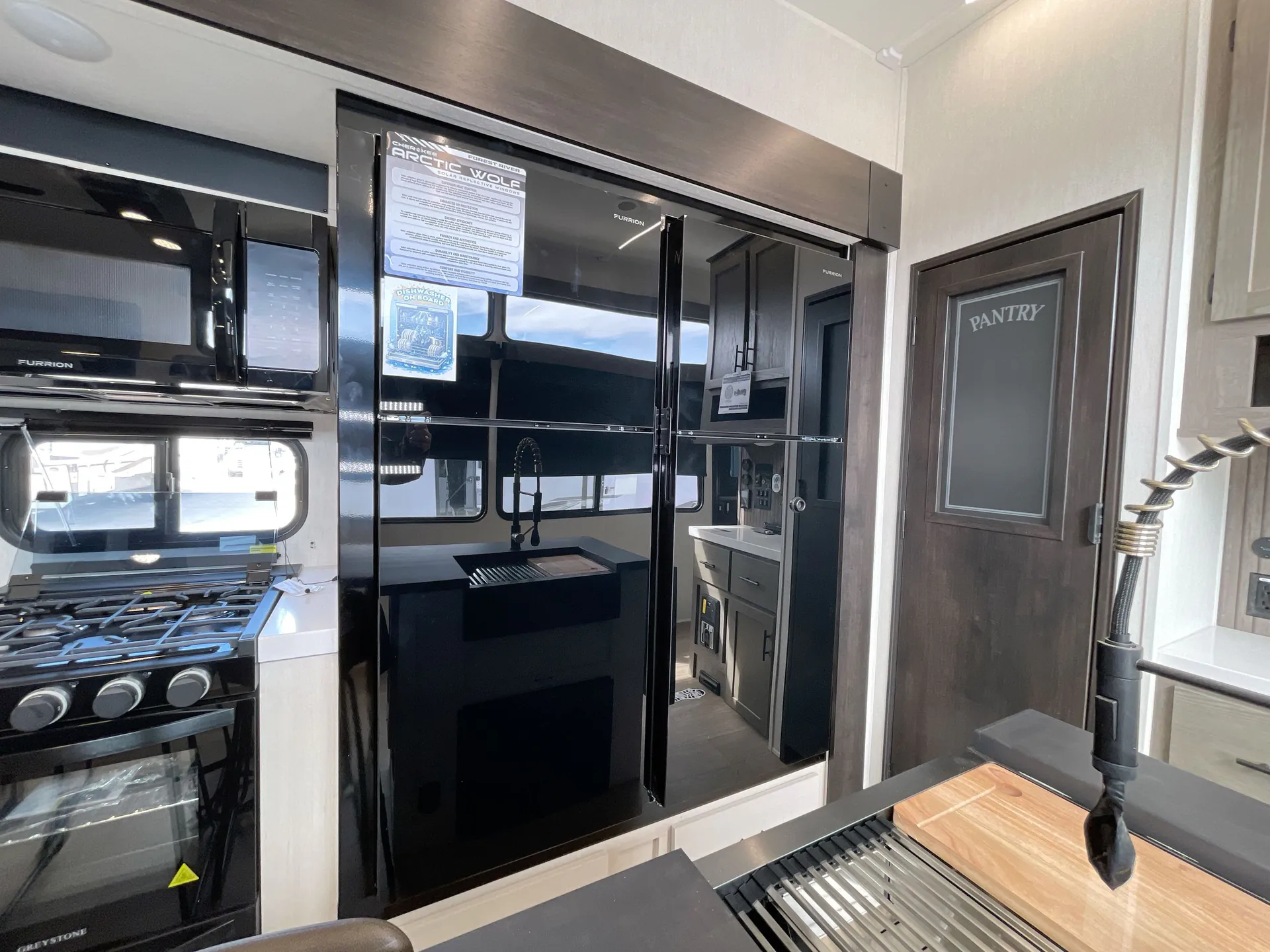 2026 Forest River Arctic Wolf 38LEAH.G — Fifth wheel kitchen showing a range, microwave, refrigerator, sink, faucet, countertop, and pantry door