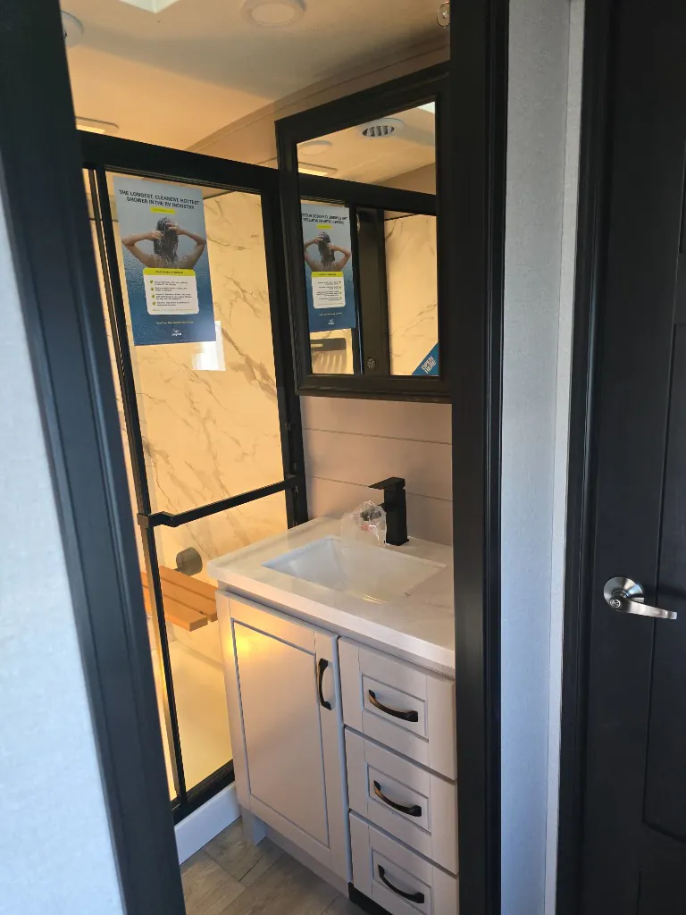 2026 Jayco North Point 377RLBH — Bathroom vanity with sink, black faucet, drawers, mirrored cabinet, and adjacent glass shower enclosure