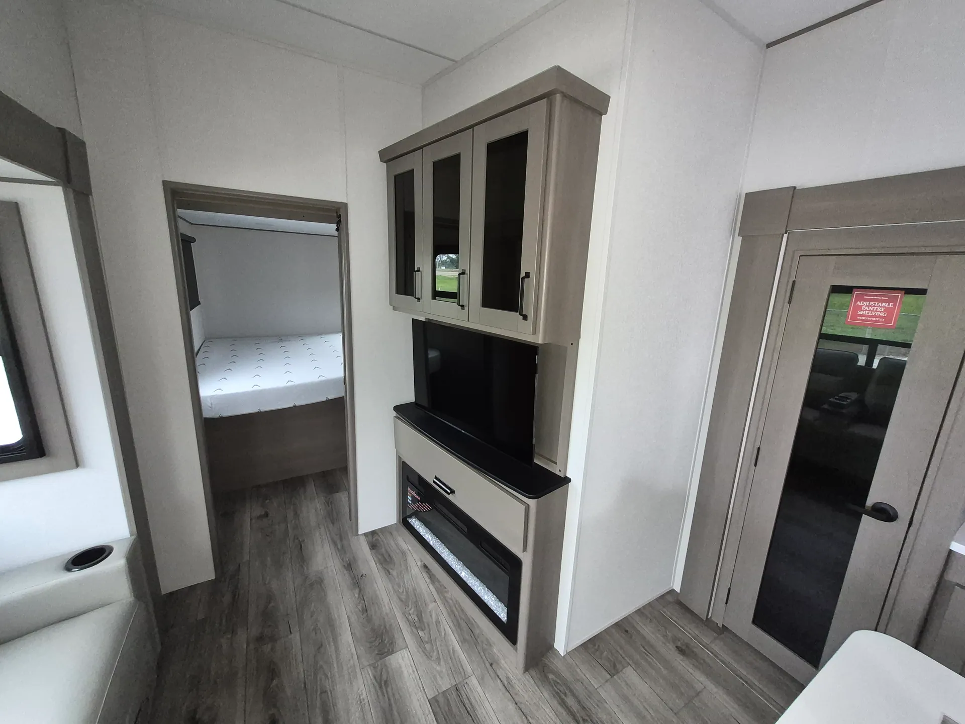 2027 Grand Design Reflection 362TBS — Living-area entertainment center with television, fireplace, and overhead cabinets beside an open doorway to the main bed