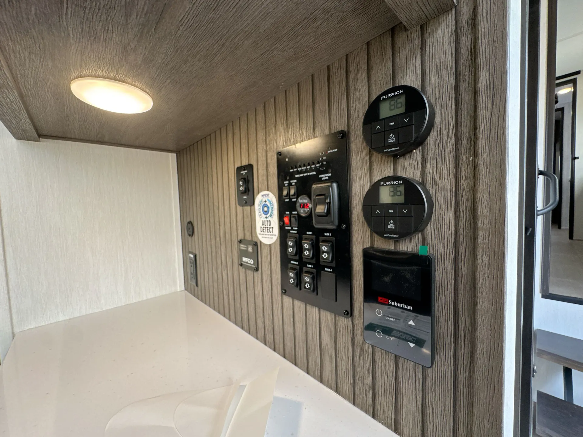 2026 Forest River Arctic Wolf 38LEAH.G — Fifth-wheel utility control panel with HVAC thermostats, power switches, and Suburban control mounted above a countertop