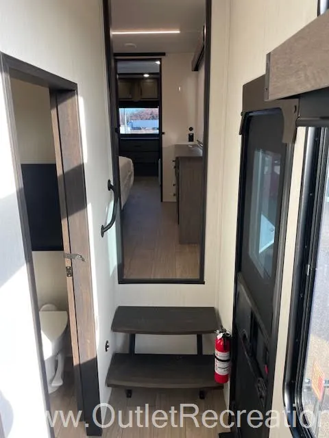 2026 Forest River Arctic Wolf 38LEAH.G — Fifth-wheel entry steps lead toward a bedroom, with a partially visible toilet compartment beside the doorway