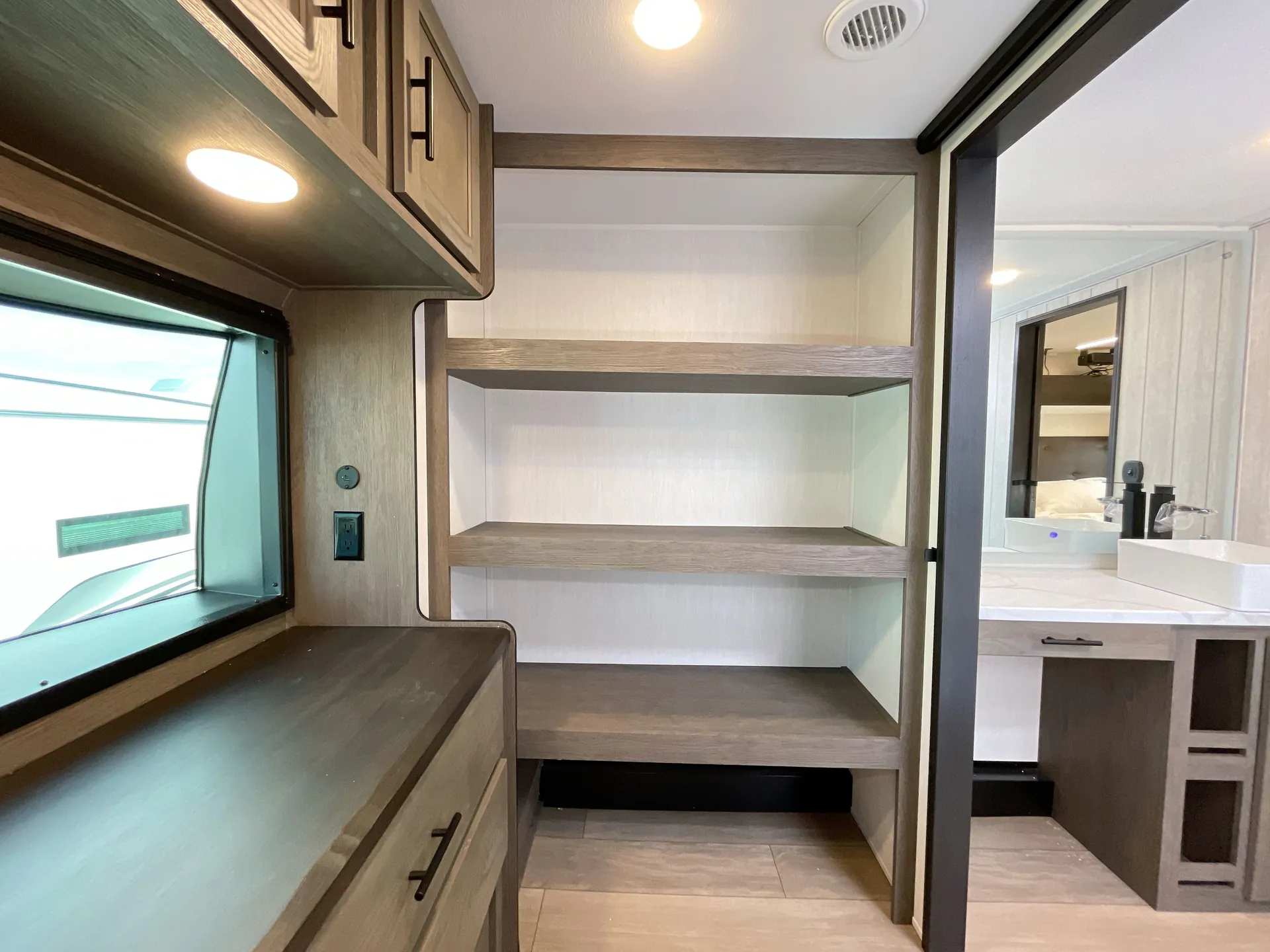 2026 Forest River Arctic Wolf 38LEAH.G — Fifth-wheel bedroom dresser and open shelving beside a doorway showing the bathroom vanity